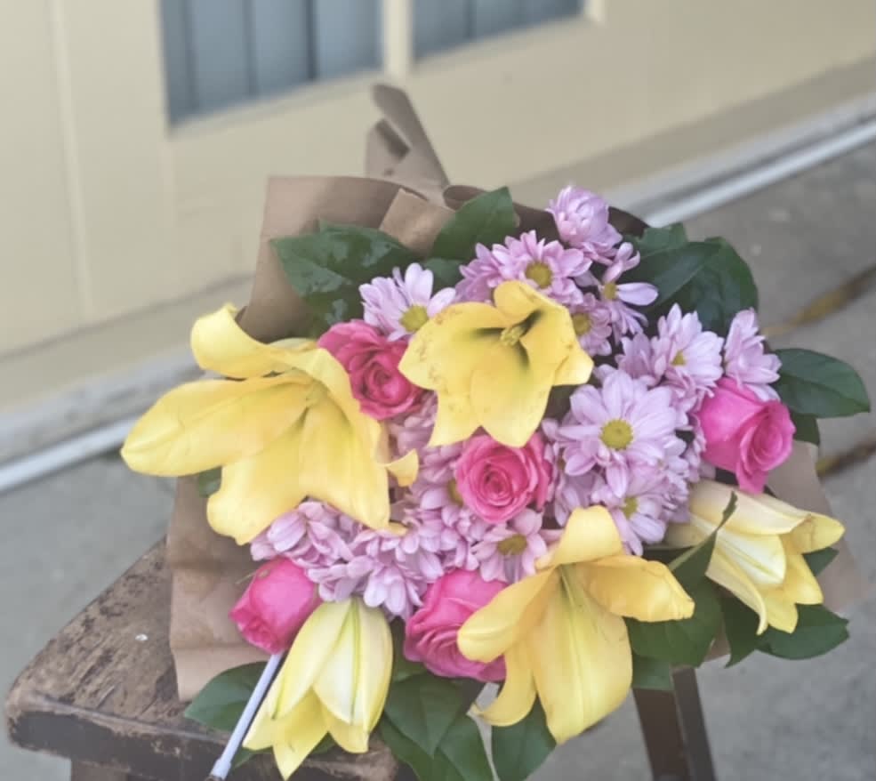 Bouquet of yellow lilies, pink roses, and lavender daisies wrapped in brown paper