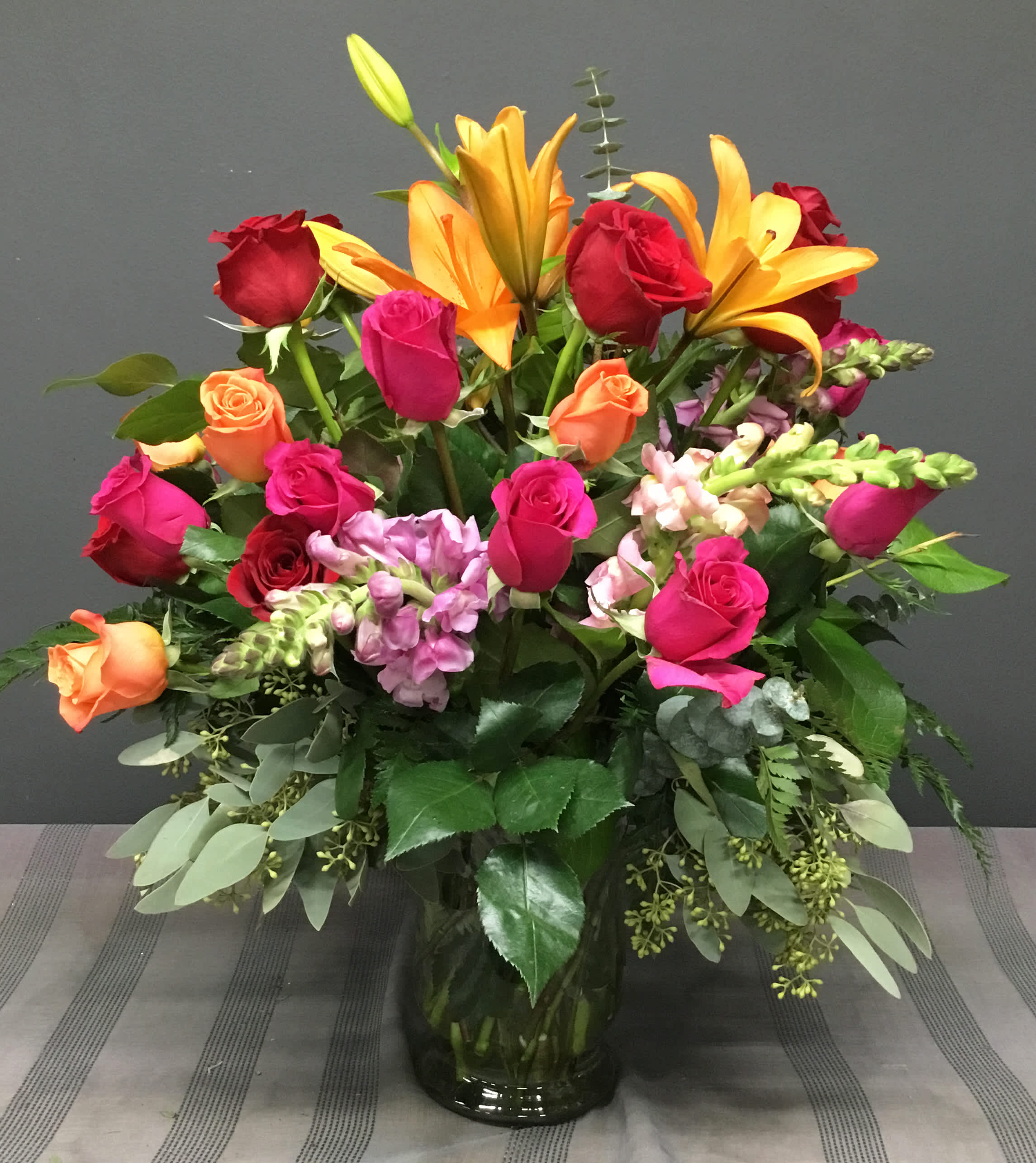 Mixed bouquet of roses, lilies, and snapdragons in a glass vase