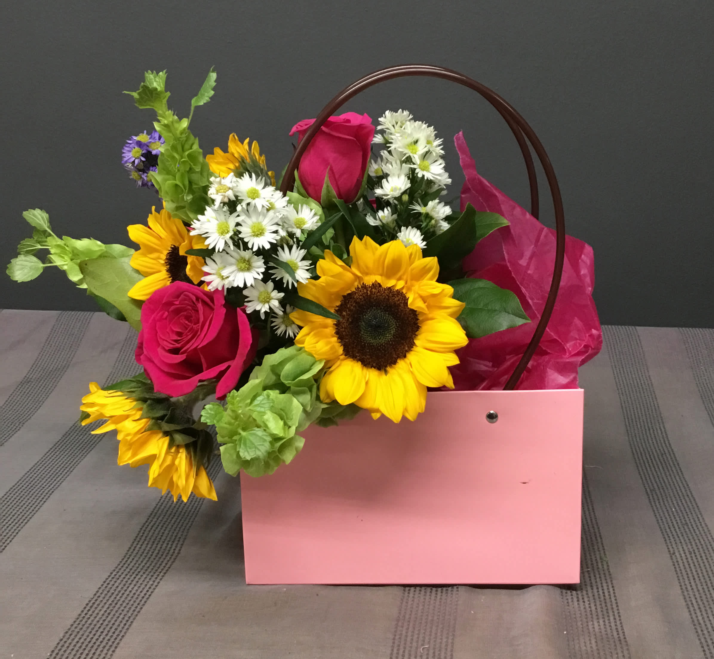 Pink gift bag with sunflowers, roses, and white daisies