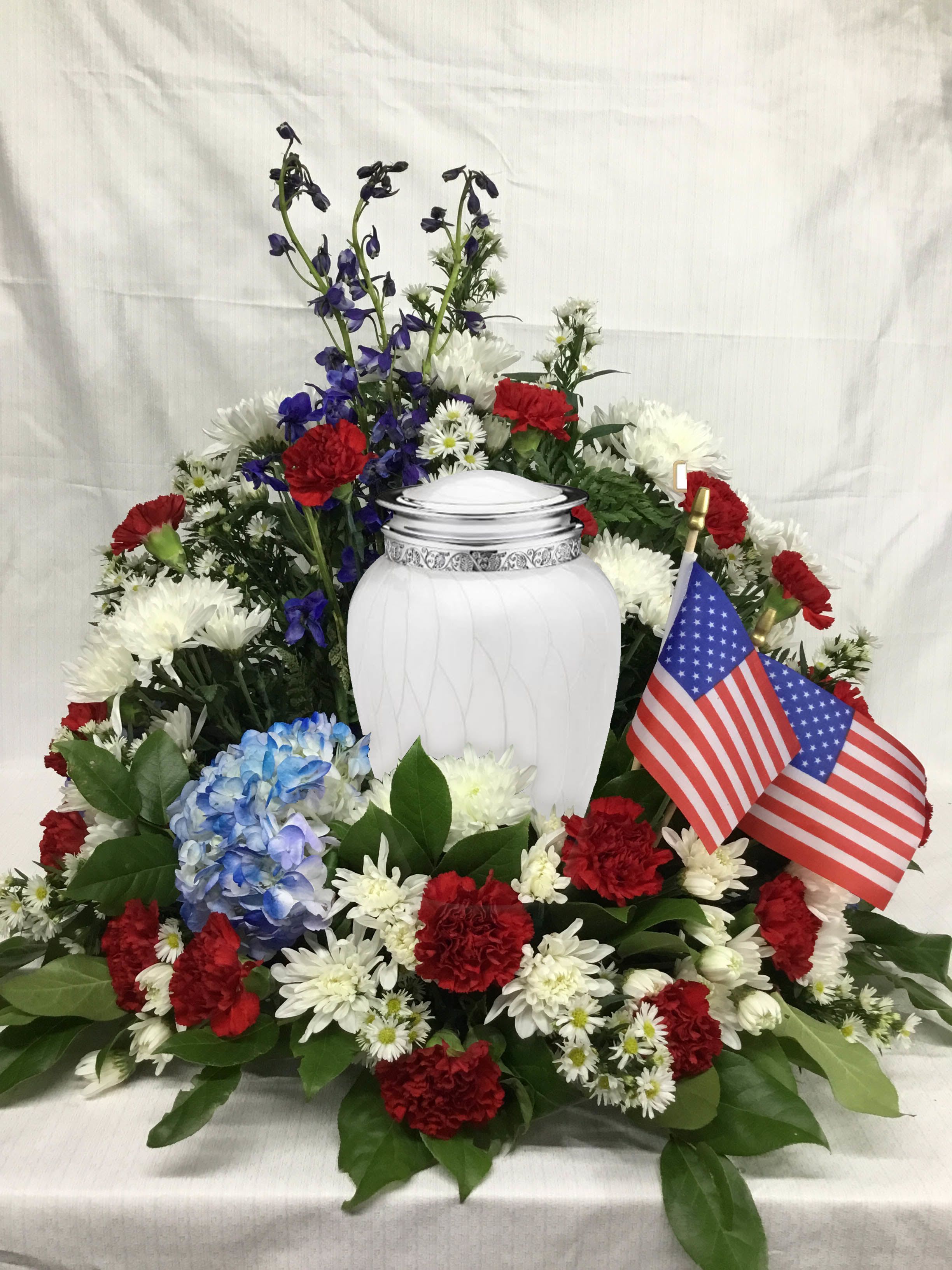 Memorial floral arrangement around a white urn with red, white, and blue flowers