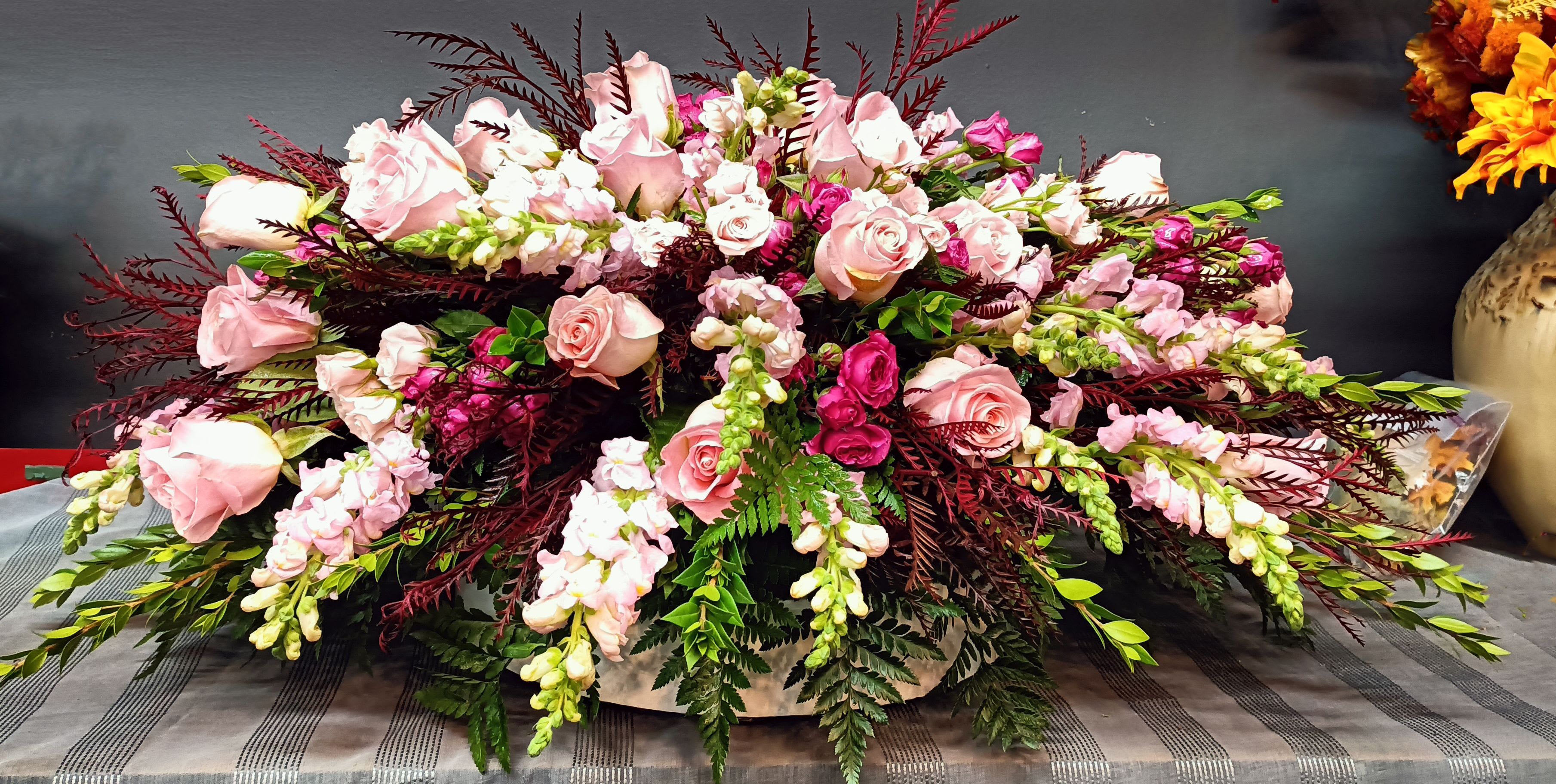 Large pink rose arrangement with burgundy foliage and white accent flowers