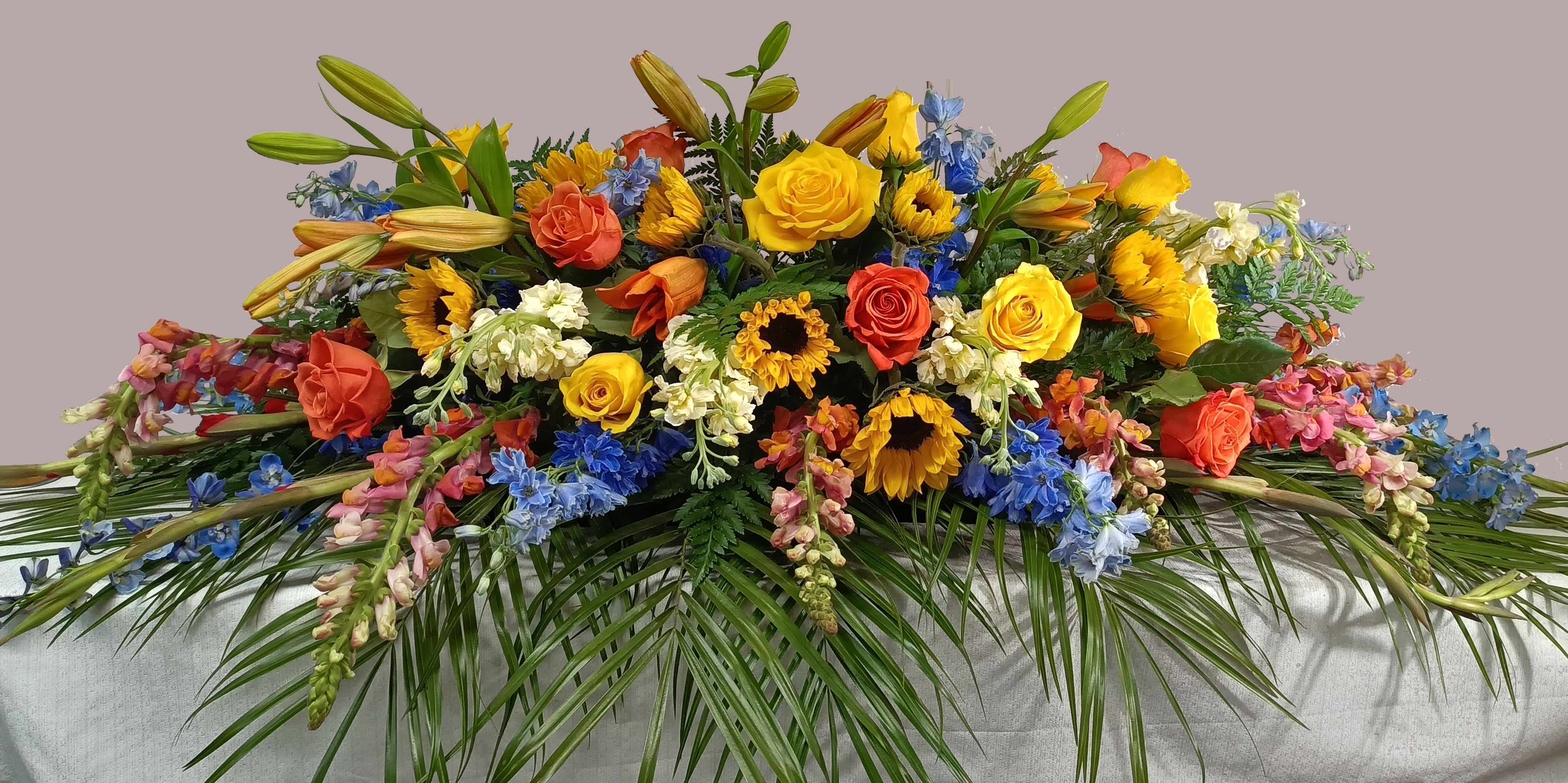 Large casket spray with yellow, orange, blue, and white flowers