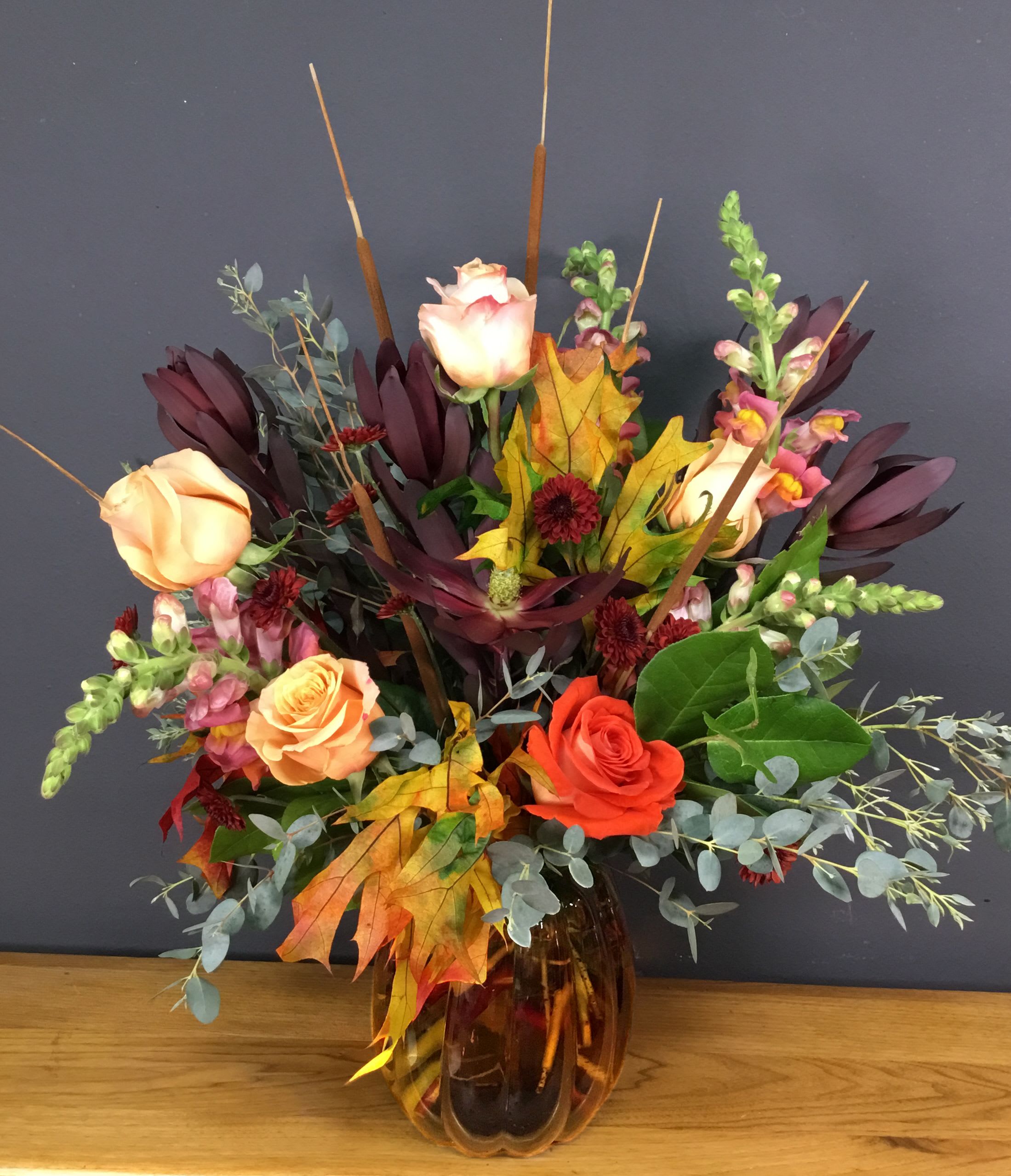 Autumn bouquet of roses and snapdragons in an amber glass vase