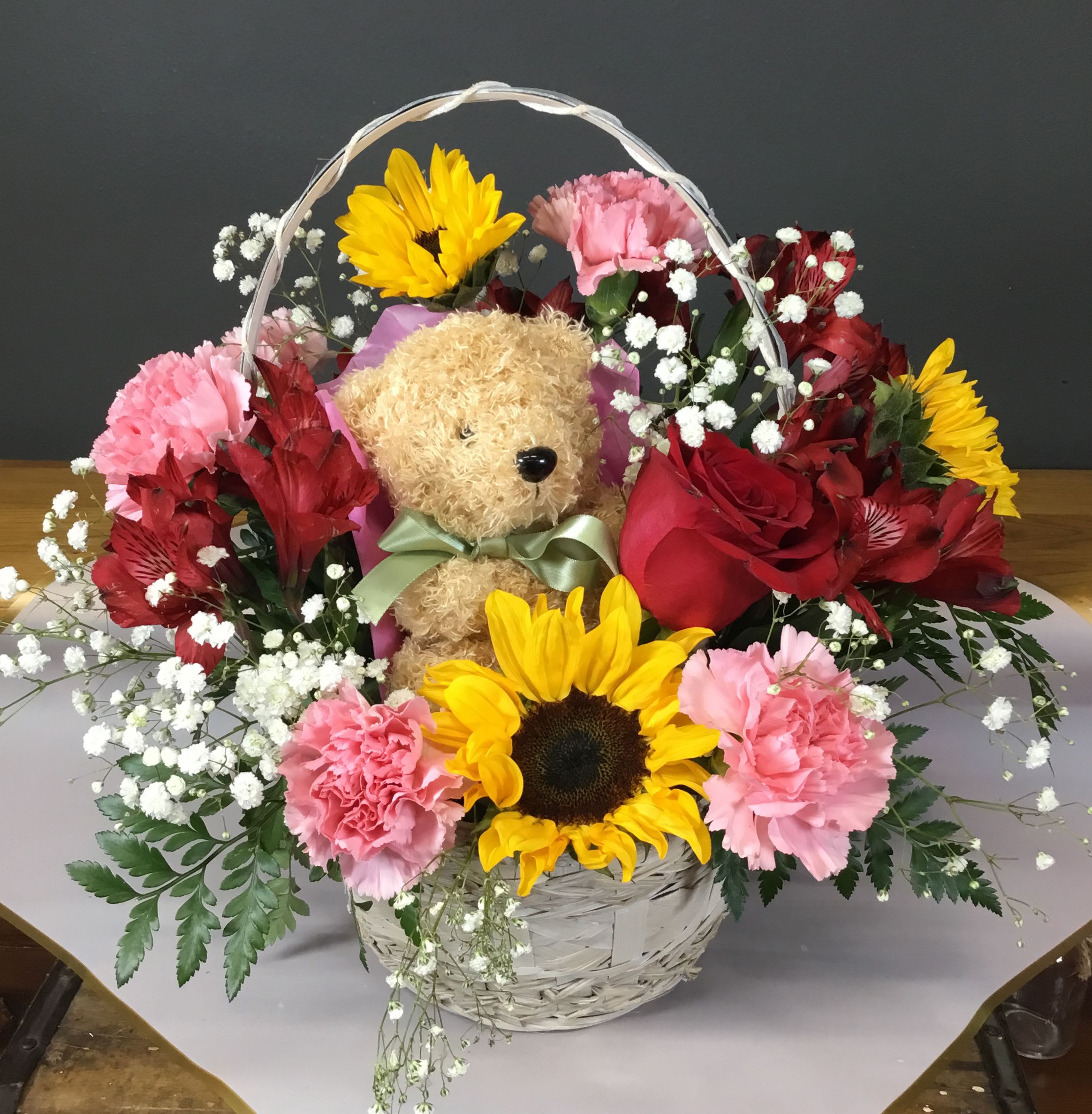 Basket arrangement with a teddy bear, sunflowers, roses, and pink carnations
