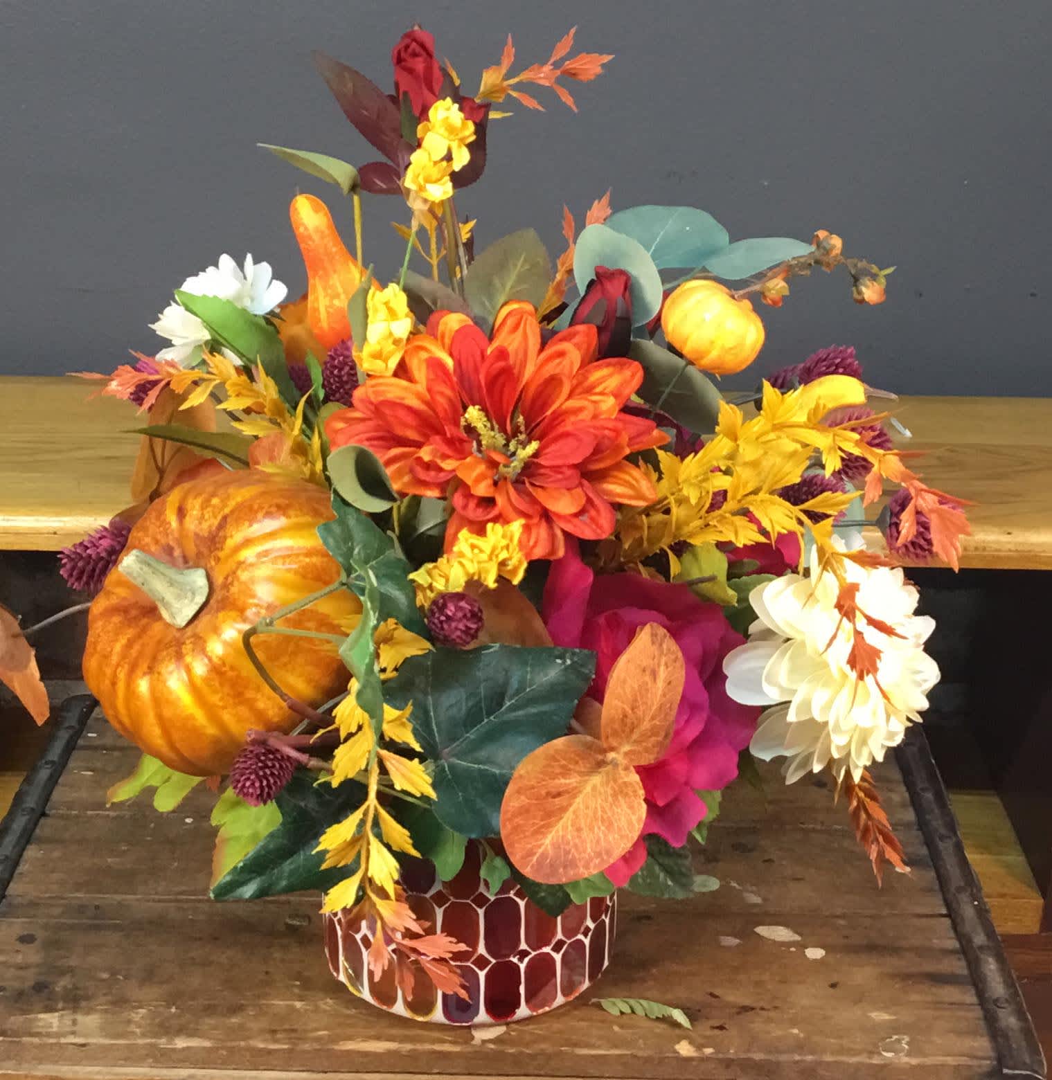 Autumn floral arrangement with pumpkins in a patterned container