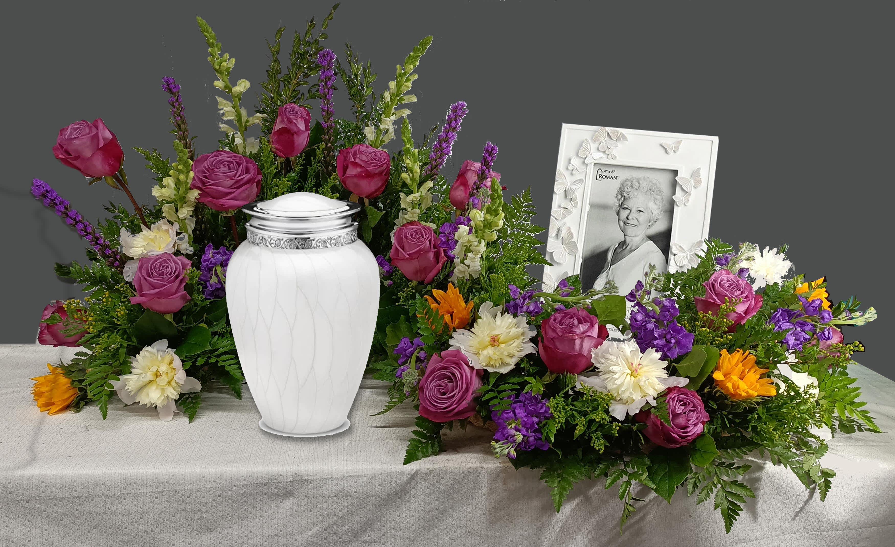 Funeral urn surrounded by purple, white, and orange flowers with a framed portrait
