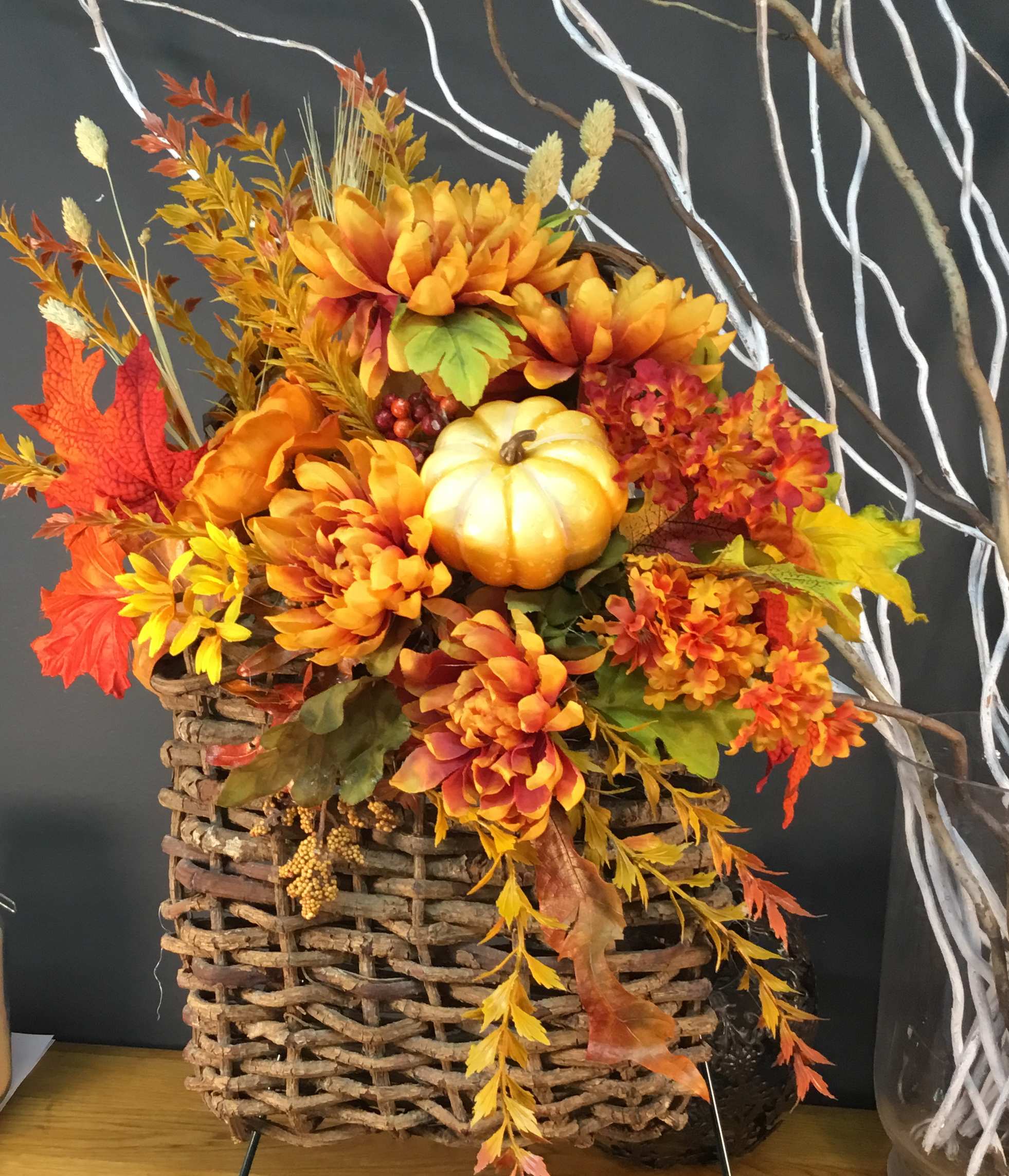 Autumn floral arrangement in a woven basket with orange flowers and a small pumpkin