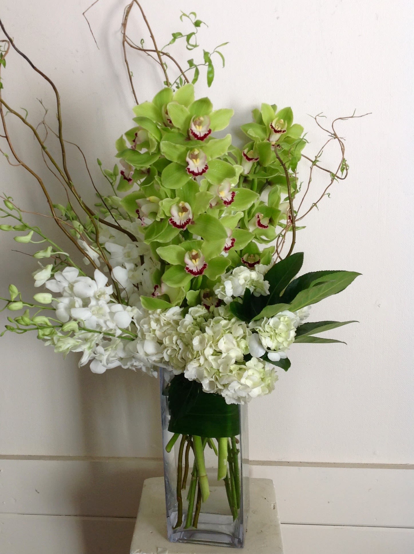 Green and white orchid arrangement in a tall glass vase