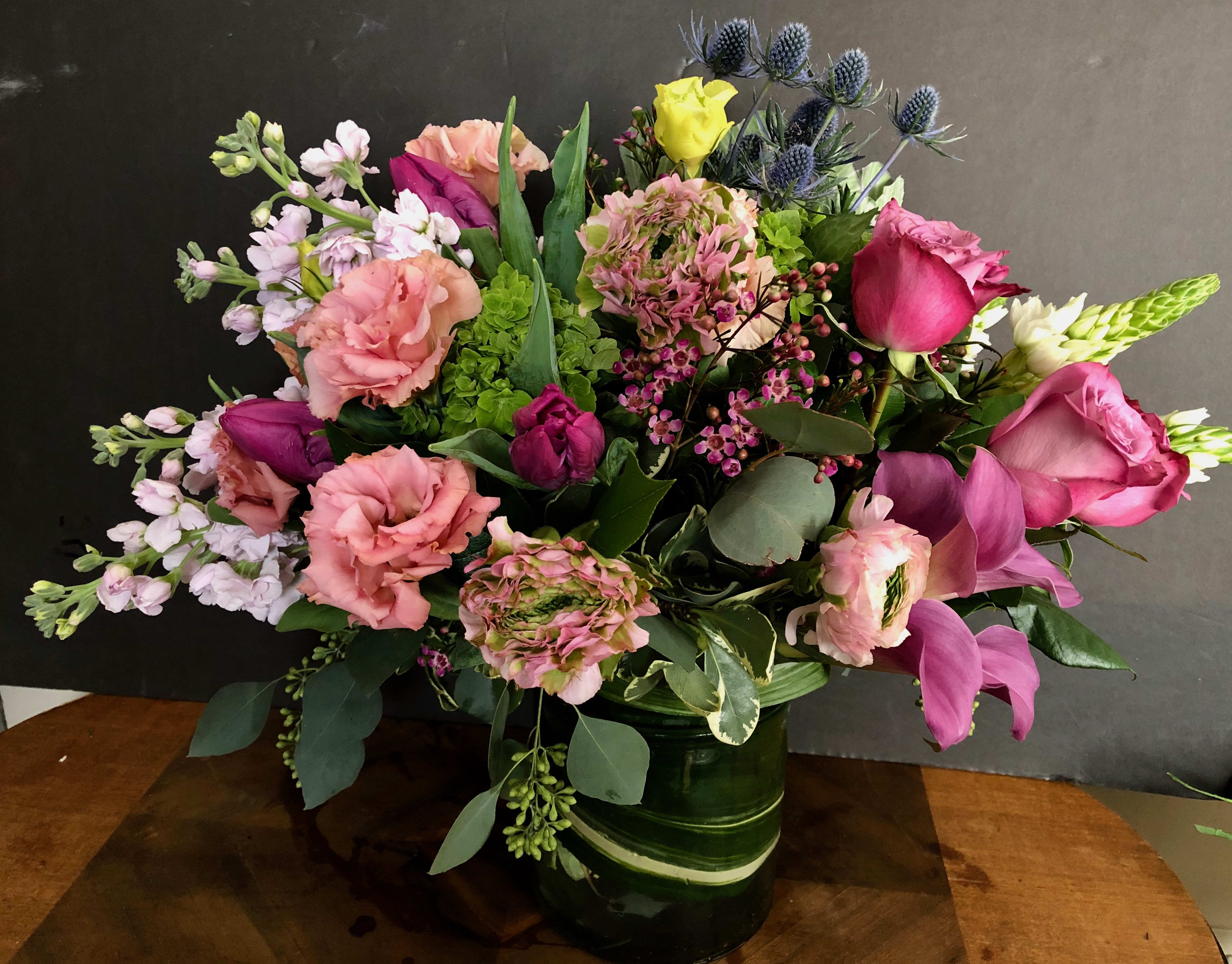Mixed bouquet of pink, purple, and yellow flowers in a green vase
