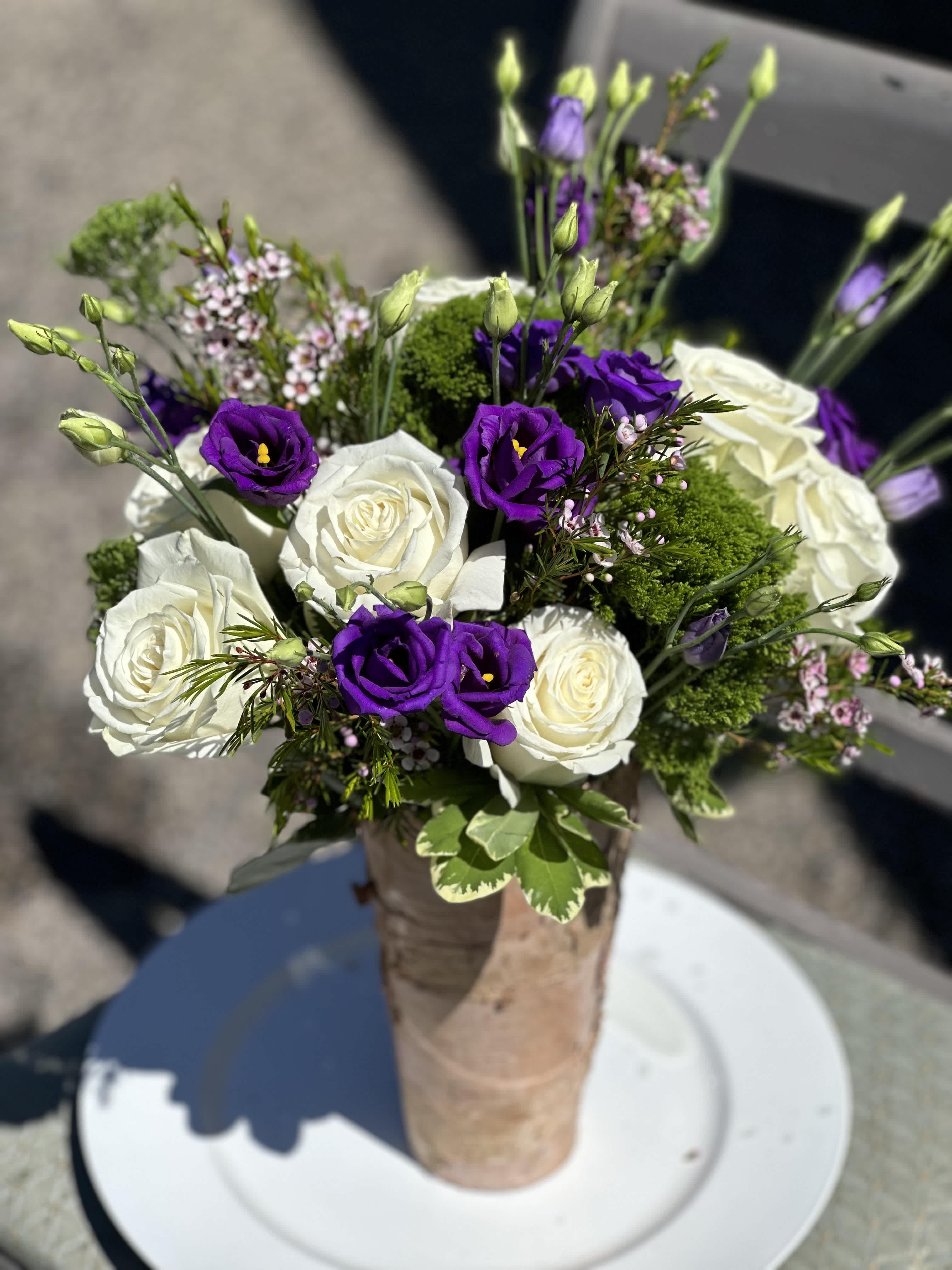 Bouquet of white roses and purple lisianthus in a wrapped vase
