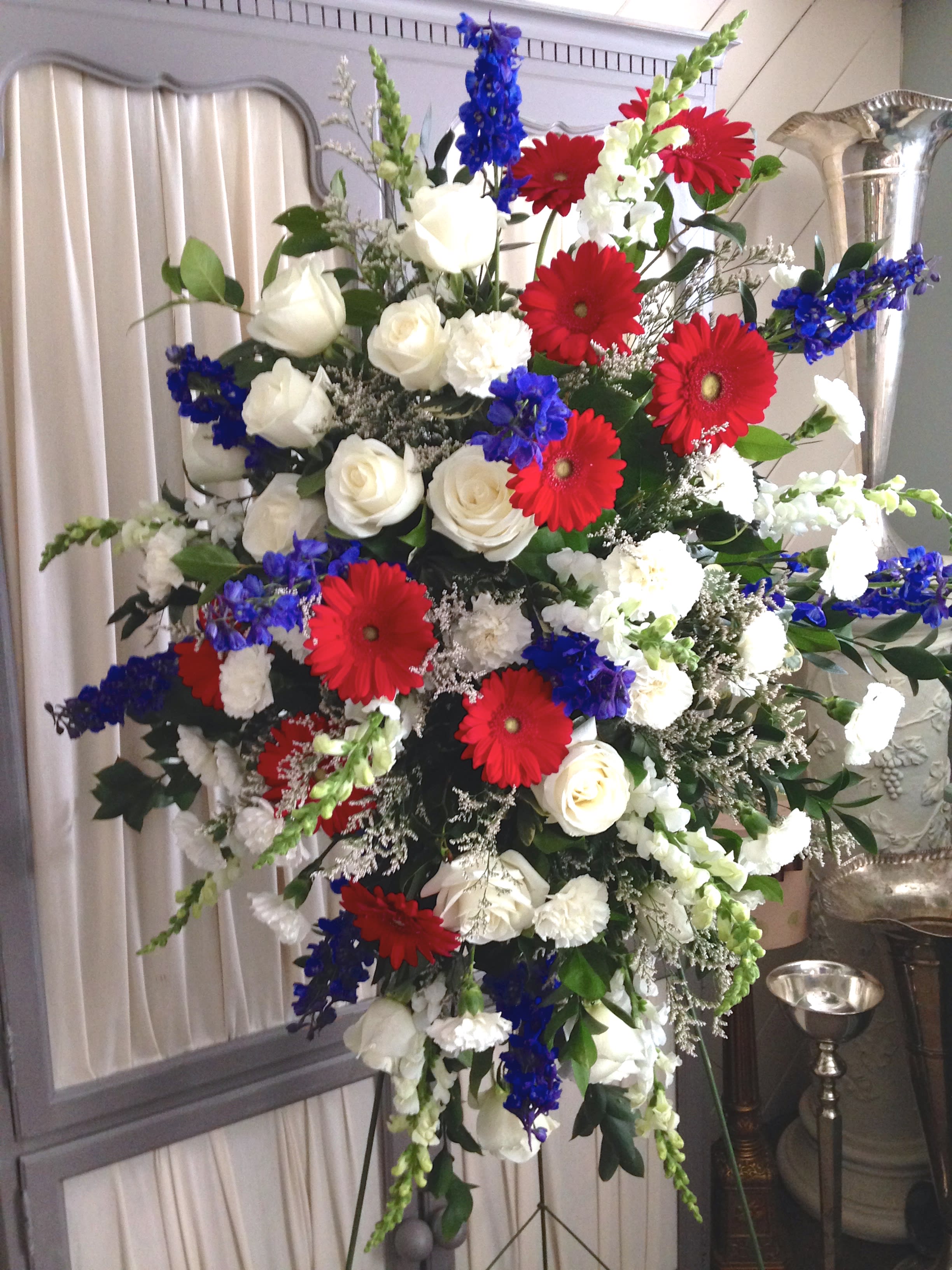 Large standing floral spray with red gerberas, white roses, and blue flowers