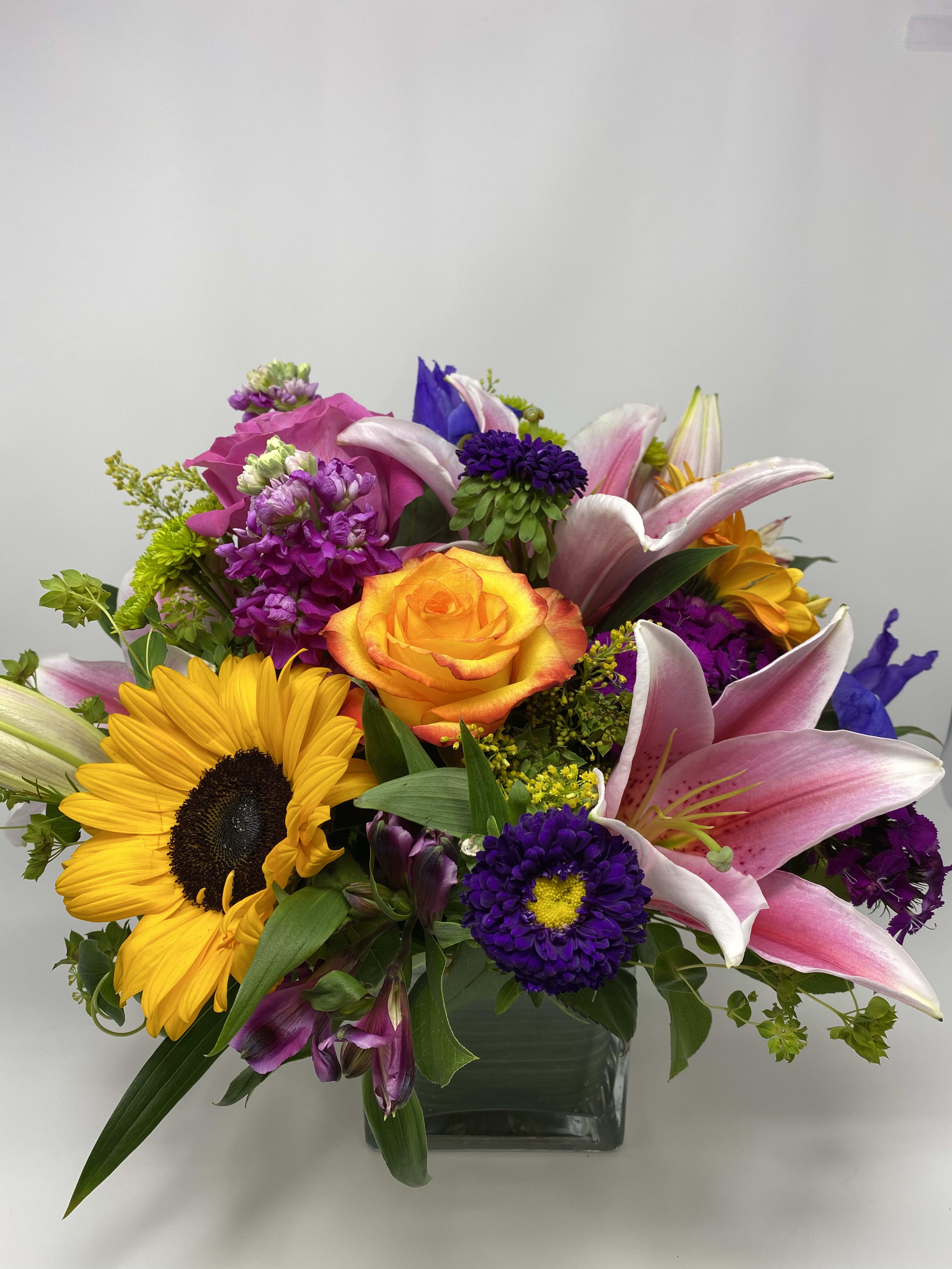 Mixed bouquet with sunflowers, pink lilies, and an orange rose in a glass vase