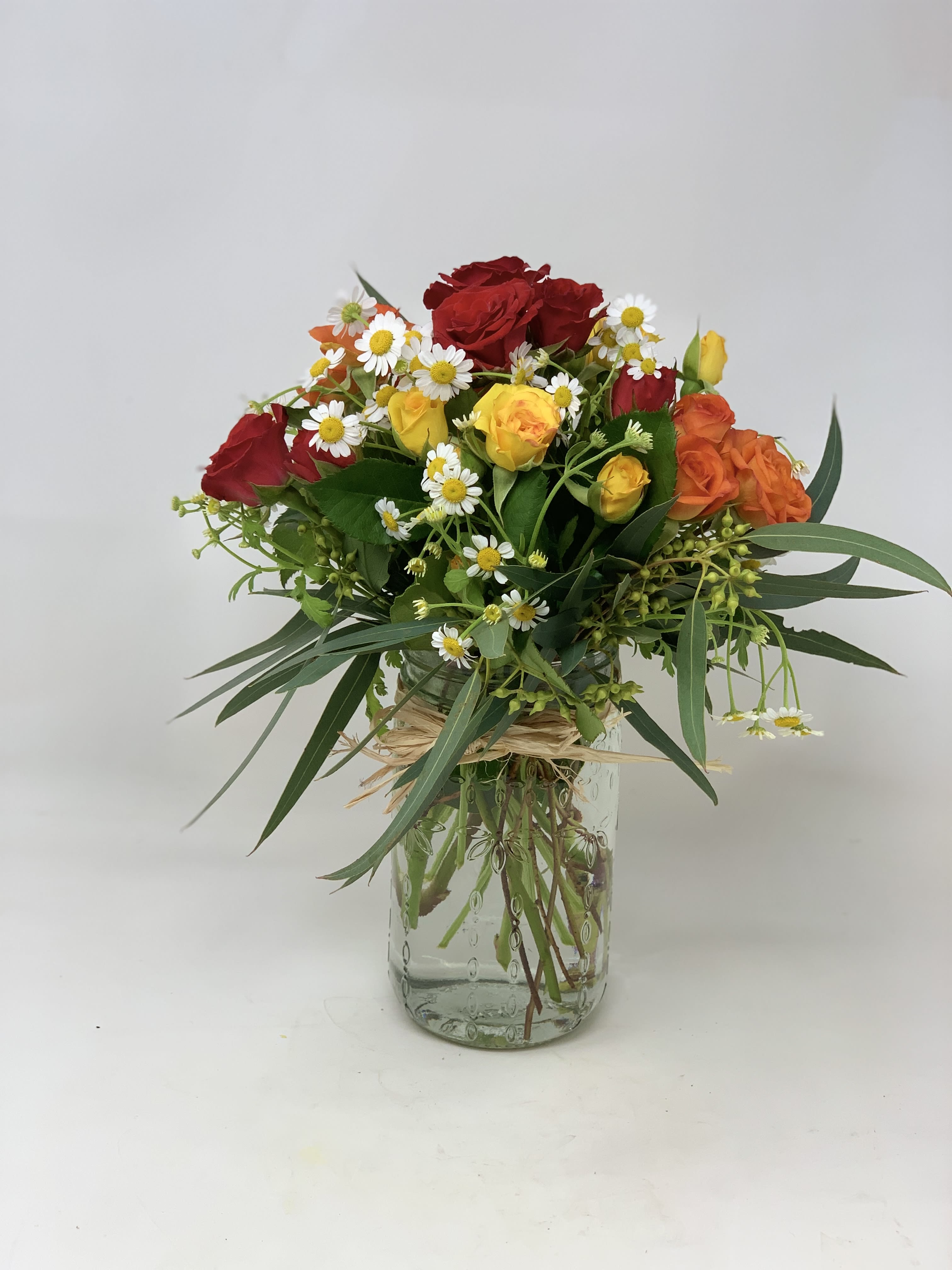 Mixed bouquet of red and yellow roses with white daisies in a glass vase