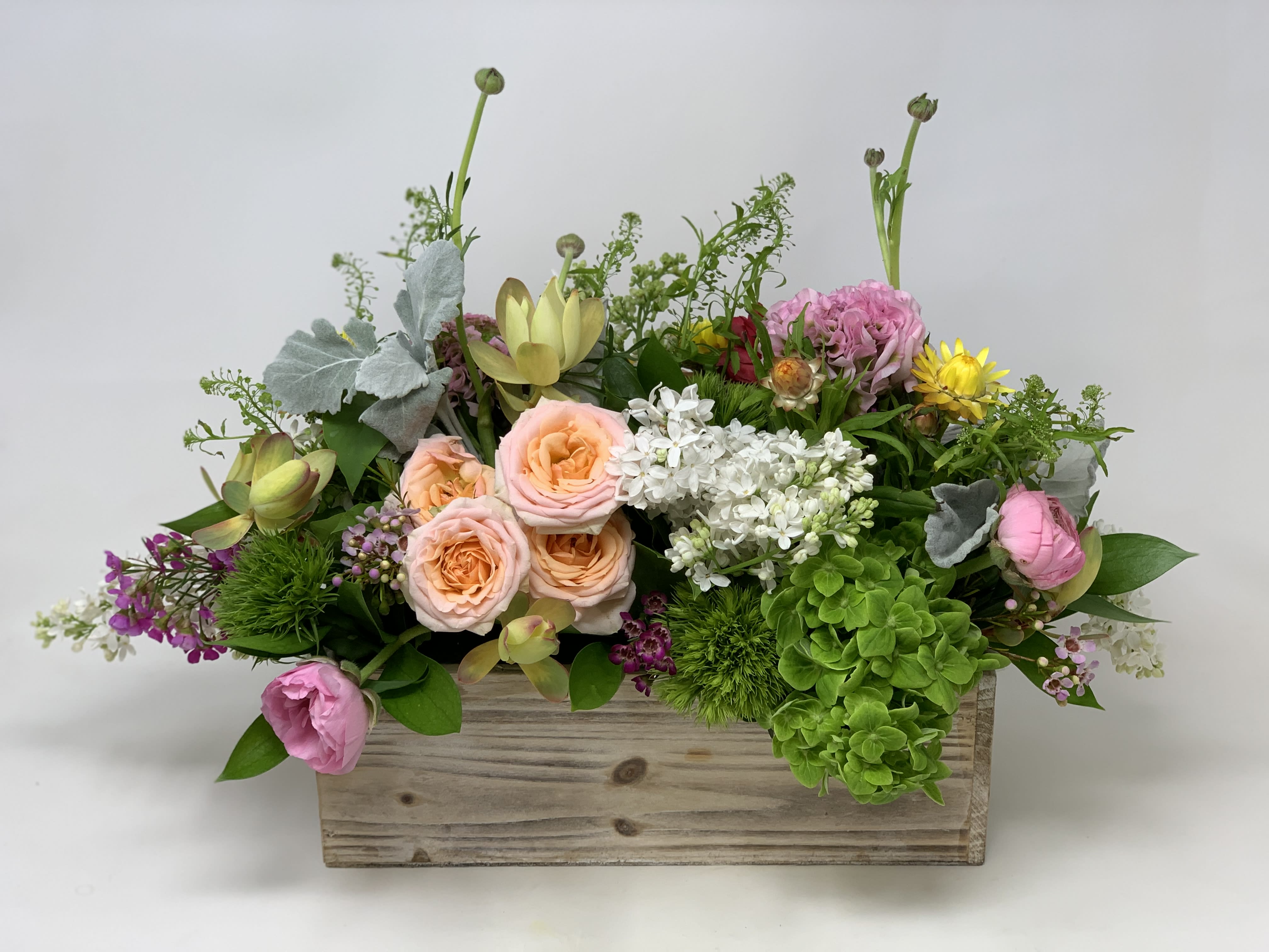 Low garden-style arrangement of mixed pastel flowers in a rustic wooden box