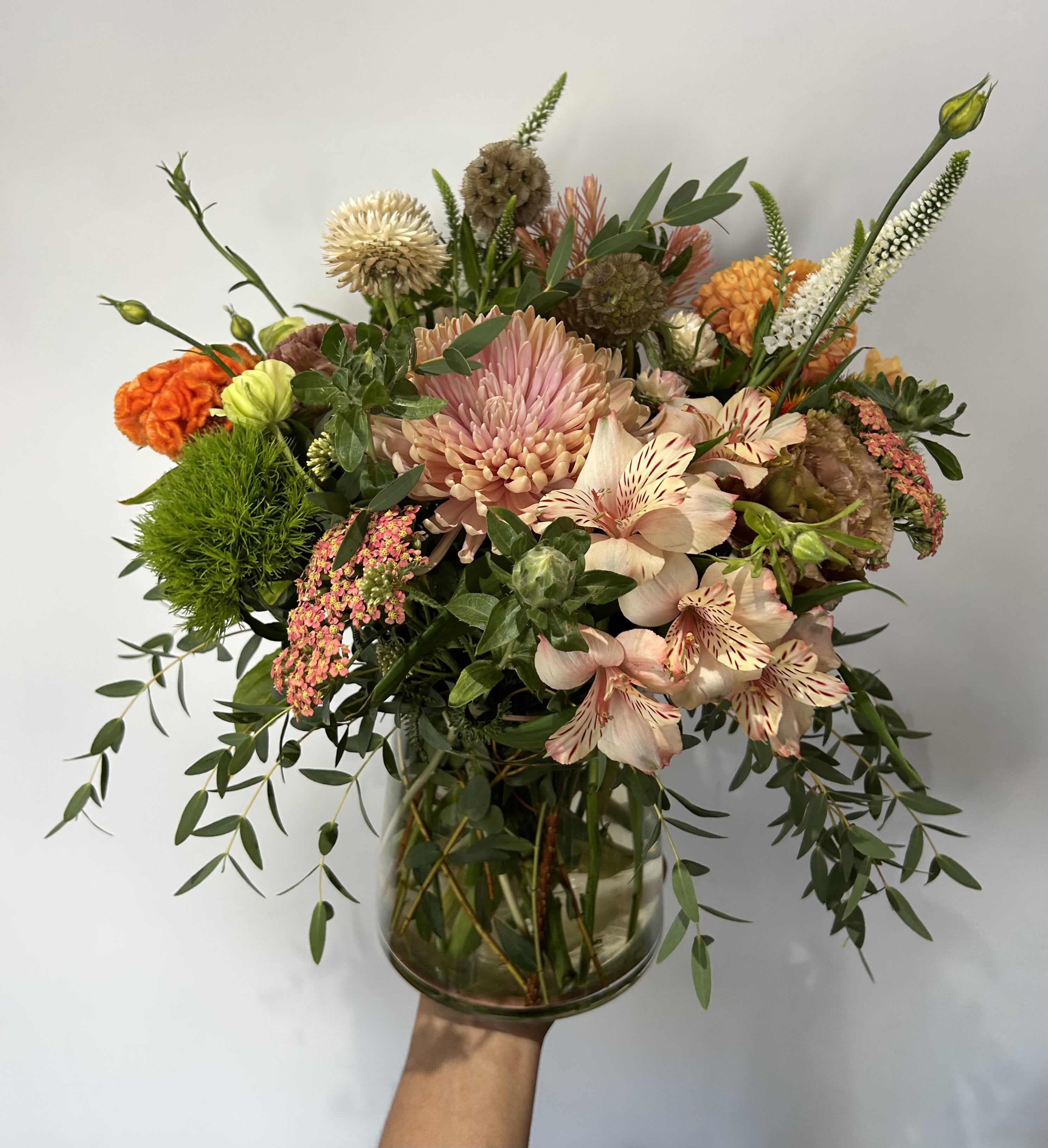 Loose peach and orange mixed flower arrangement with green accents in a clear glass vase