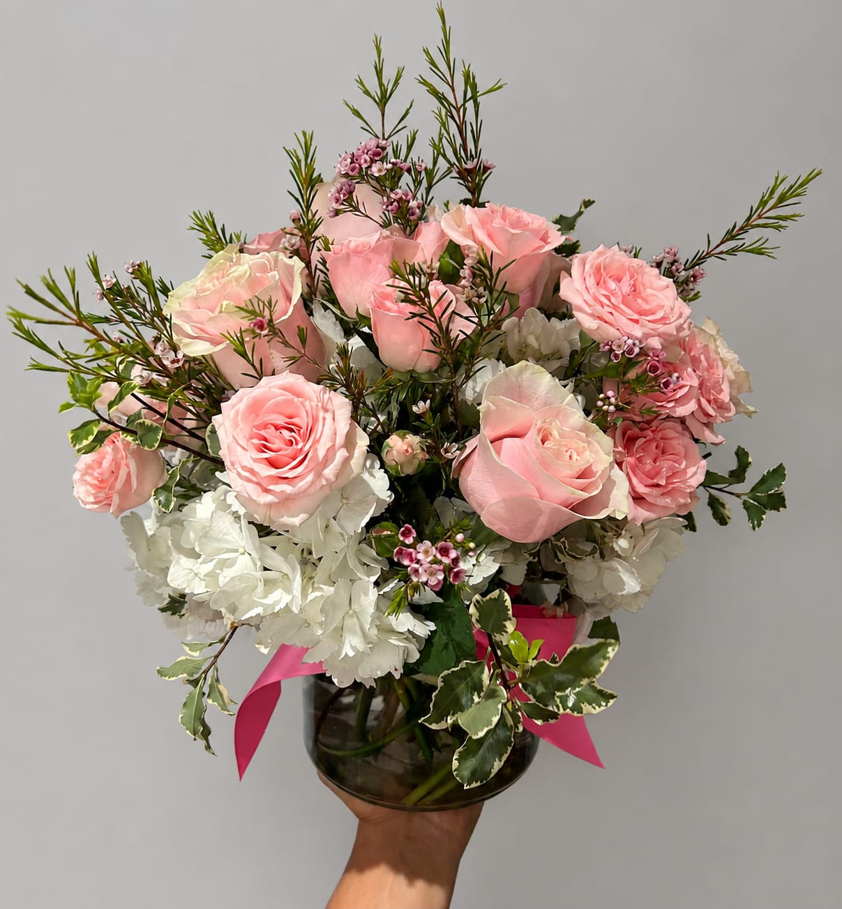 Pink roses and white hydrangeas in a glass vase with a pink ribbon
