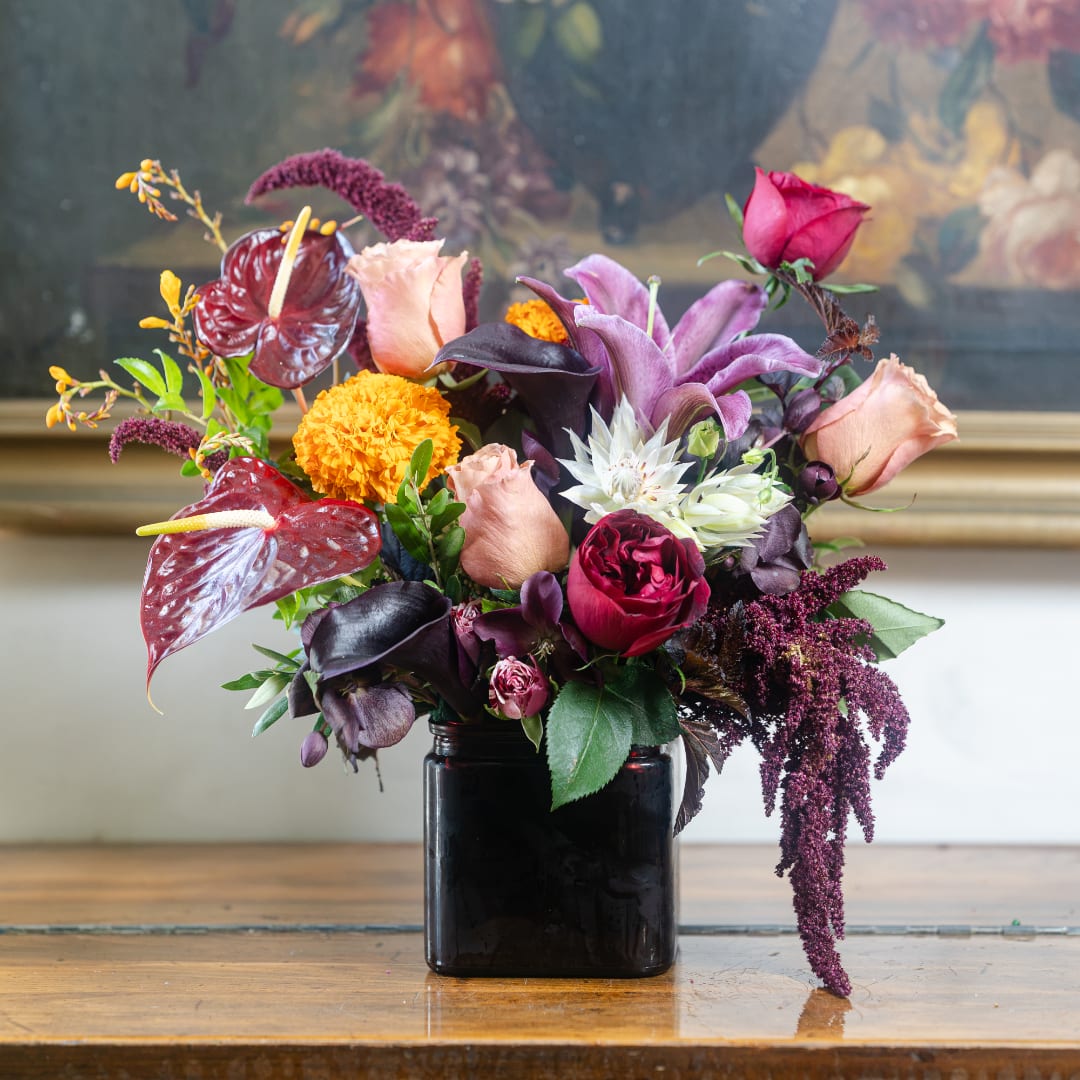 Mixed bouquet in a black vase with roses, lilies, and orange blooms