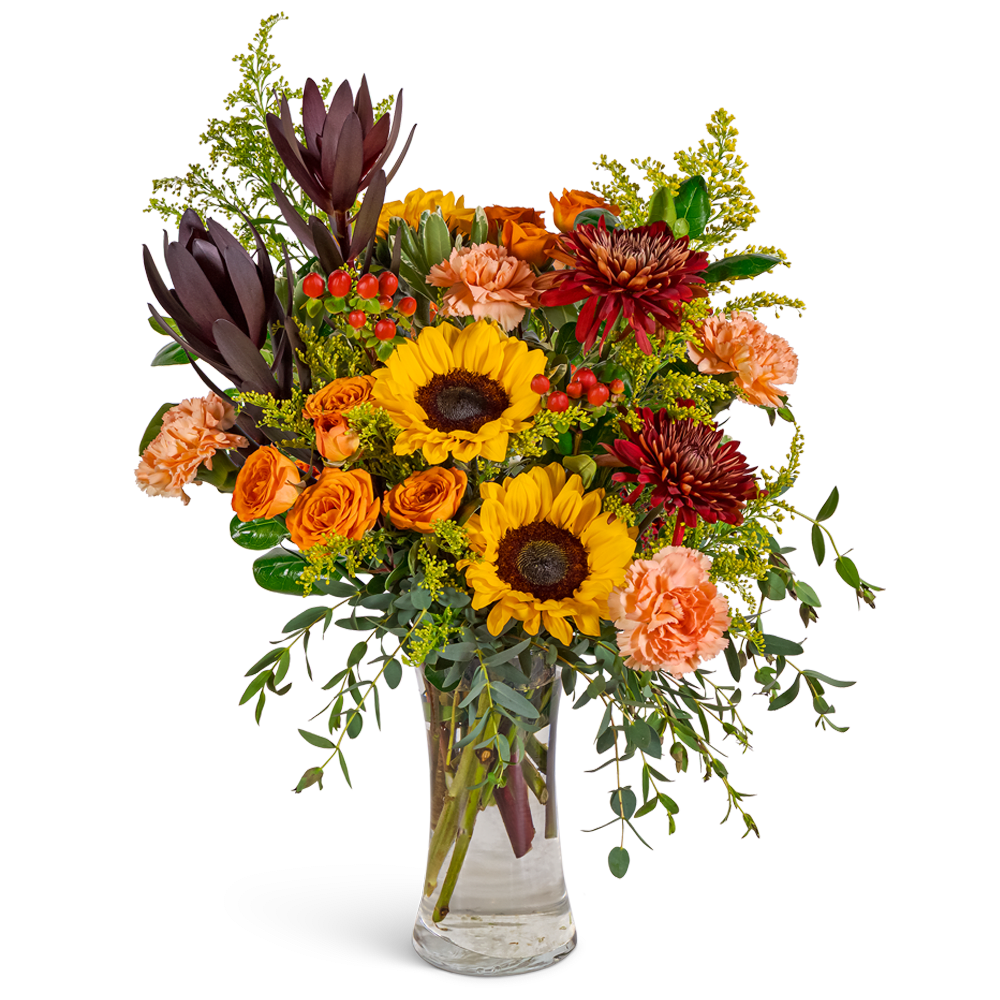 Bouquet of sunflowers, orange roses, and carnations in a clear glass vase