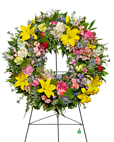 Large floral wreath on a stand with yellow lilies, roses, and mixed blooms