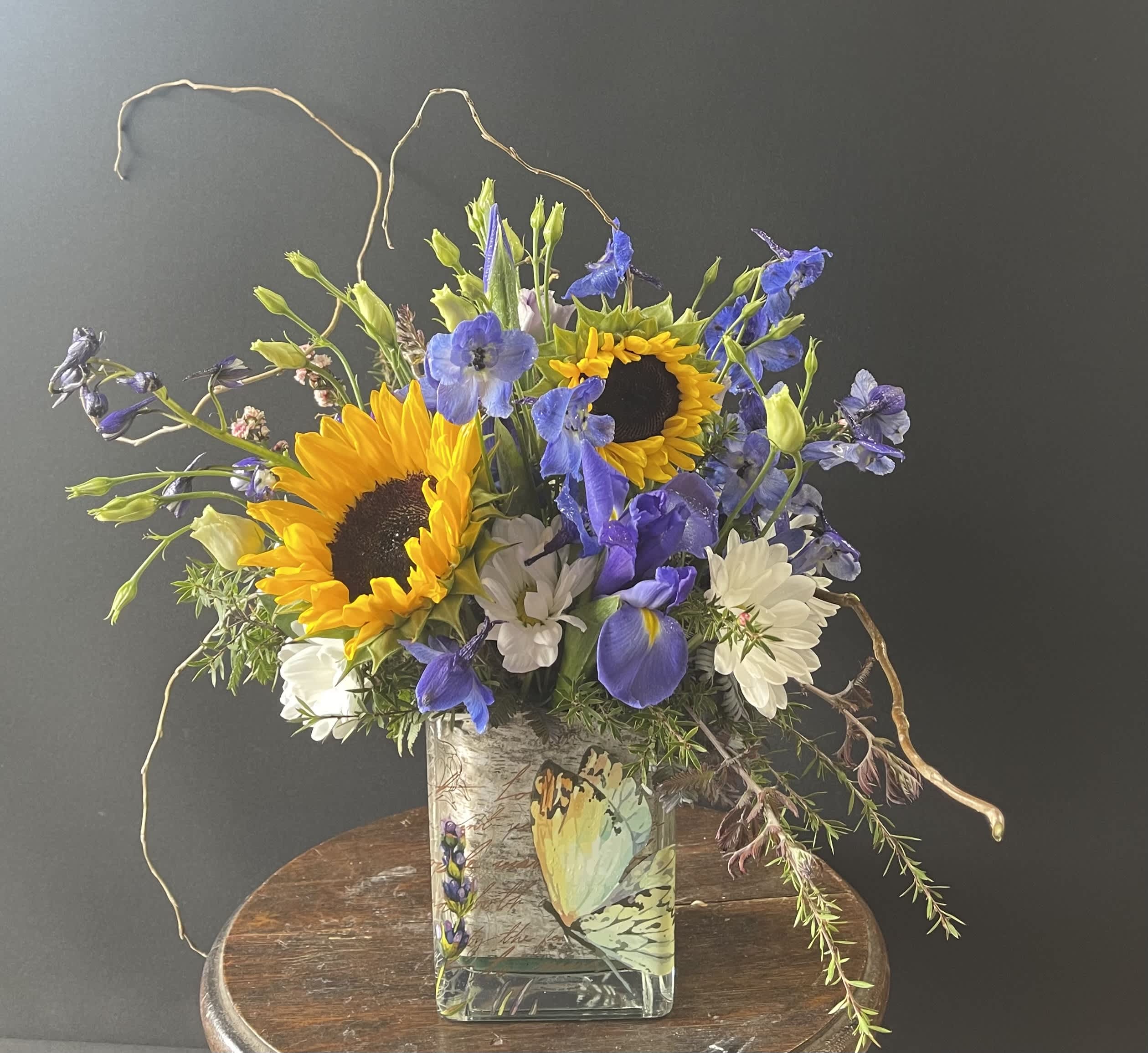 Bouquet of sunflowers, blue flowers, and white daisies in a glass vase