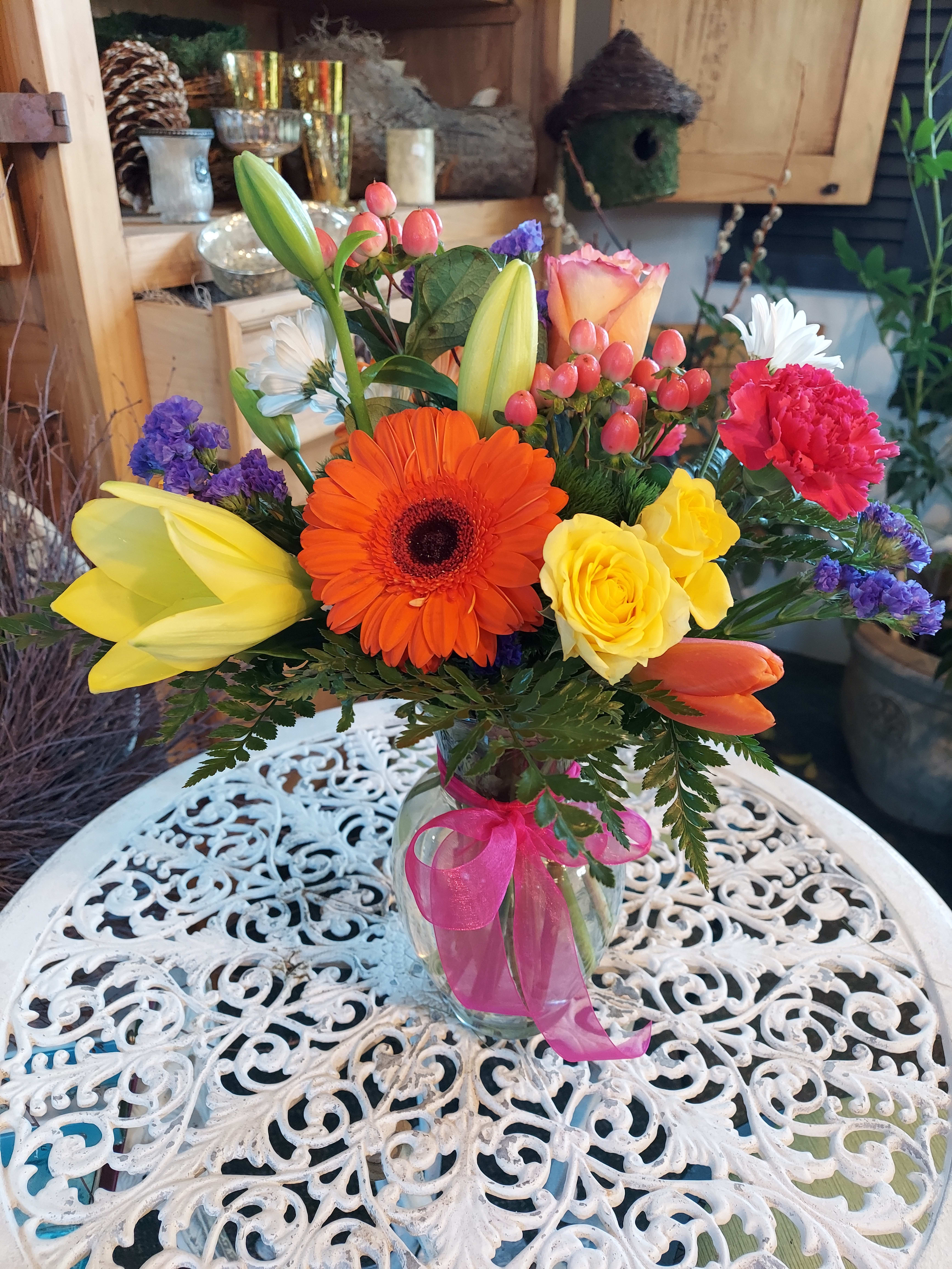 Colorful mixed bouquet in a glass vase with a pink ribbon