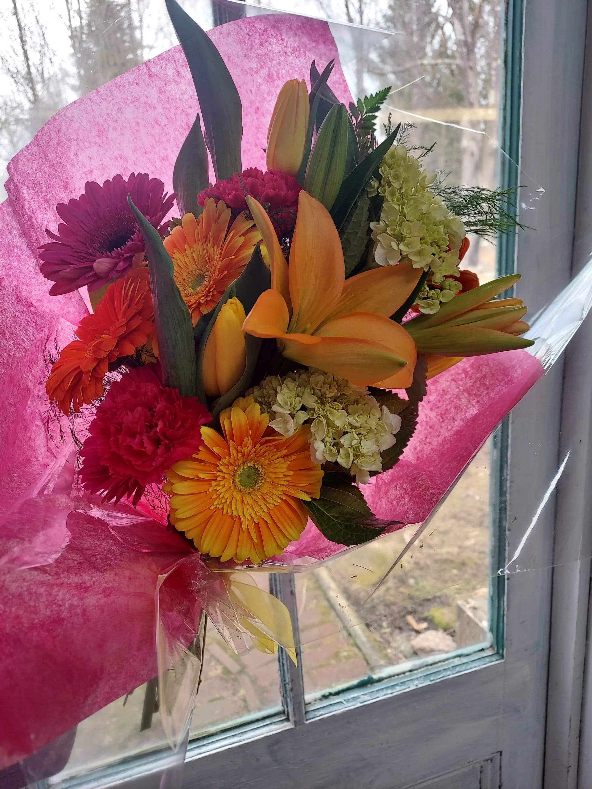 Bouquet of orange lilies, gerbera daisies, and pink chrysanthemums wrapped in pink paper