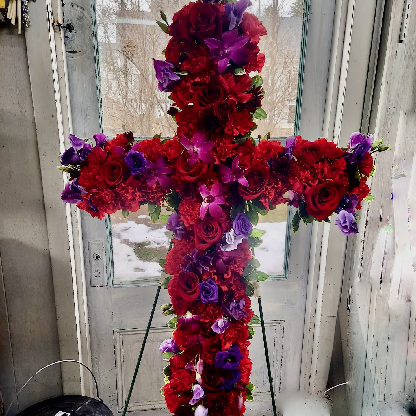 Cross-shaped floral arrangement of red and purple flowers on a stand