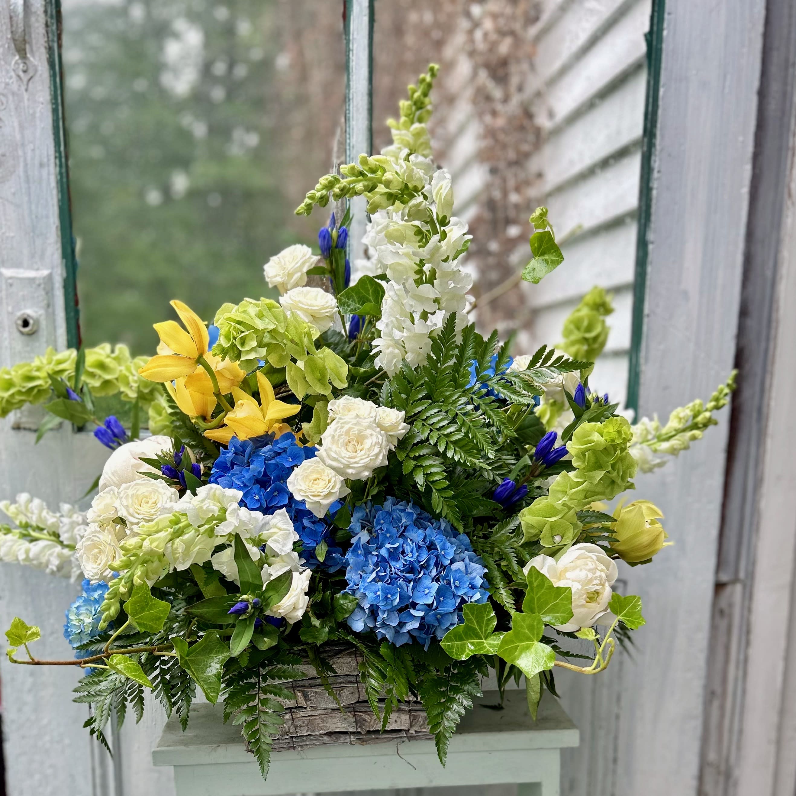 Mixed bouquet with blue hydrangeas, white roses, and yellow lilies in a basket