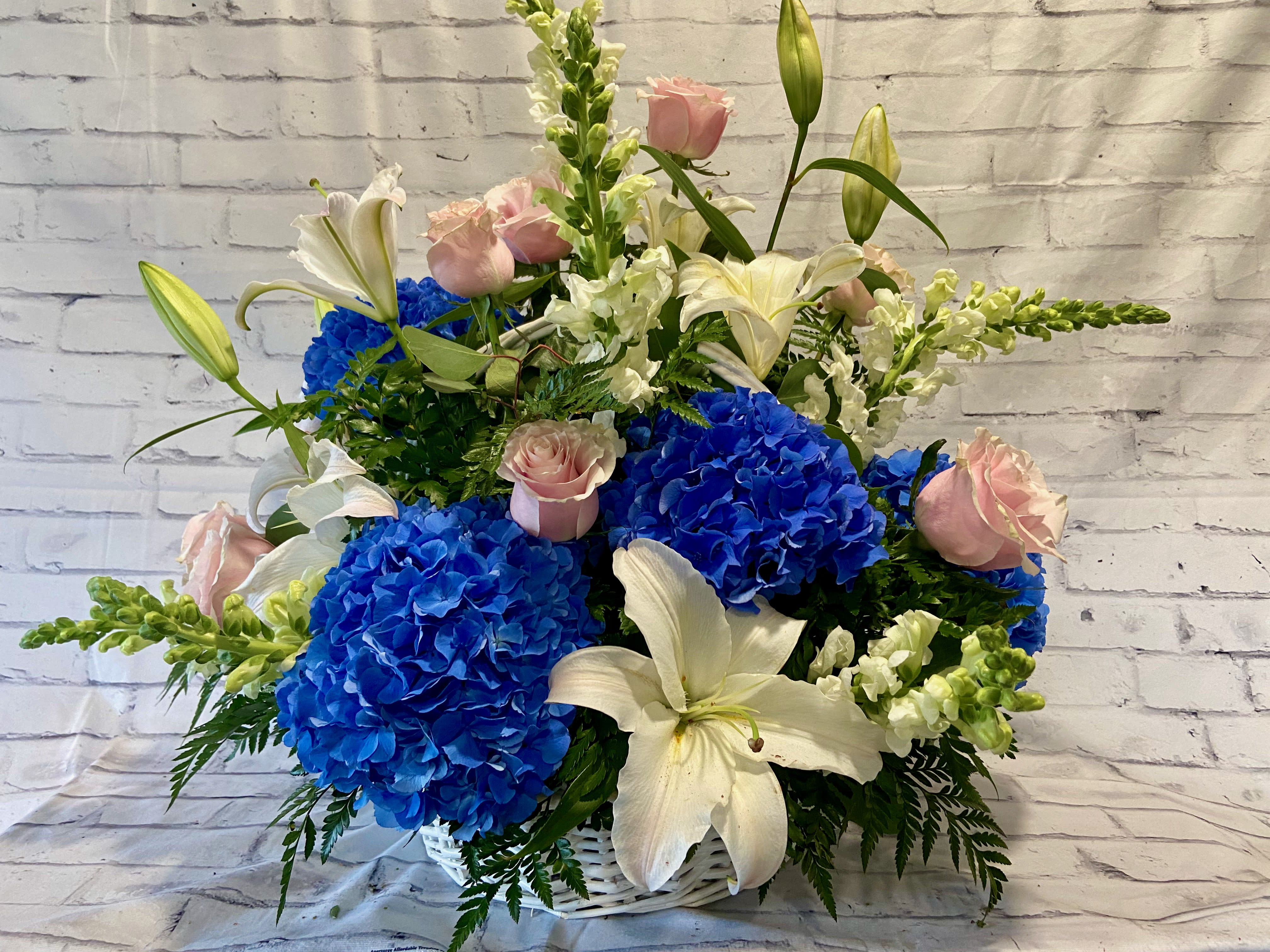 Blue hydrangeas and white lilies with pink roses in a white basket