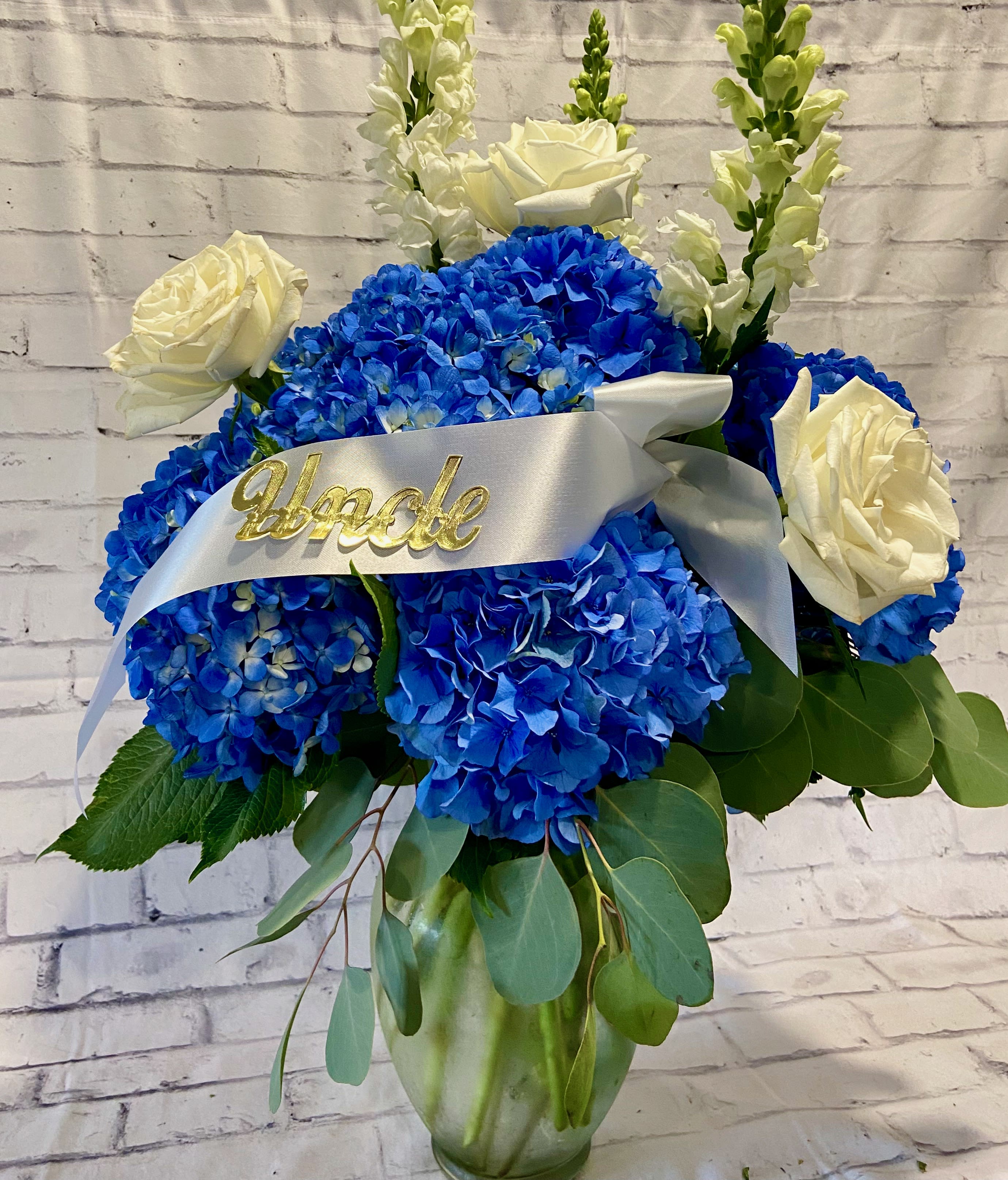 Blue hydrangea and white rose arrangement in a glass vase with a white ribbon