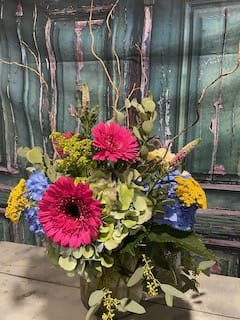 Bright mixed bouquet with pink gerbera daisies and blue and yellow blooms in a vase