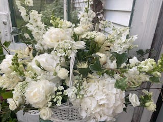 White floral arrangement with roses, hydrangeas, and snapdragons in a basket