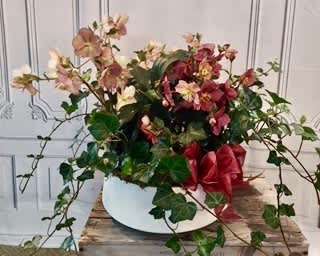 Pink and red flowers arranged in a white bowl with trailing ivy