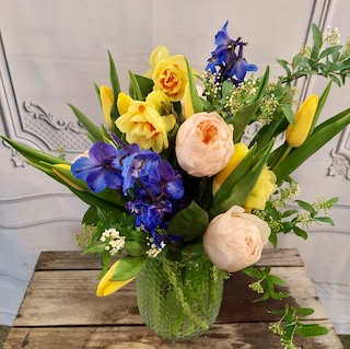 Mixed bouquet in a green glass vase with yellow, blue, and peach flowers