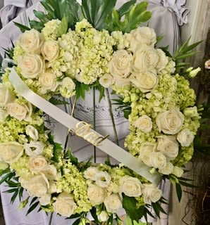 White floral wreath with roses and pale green blooms on a stand