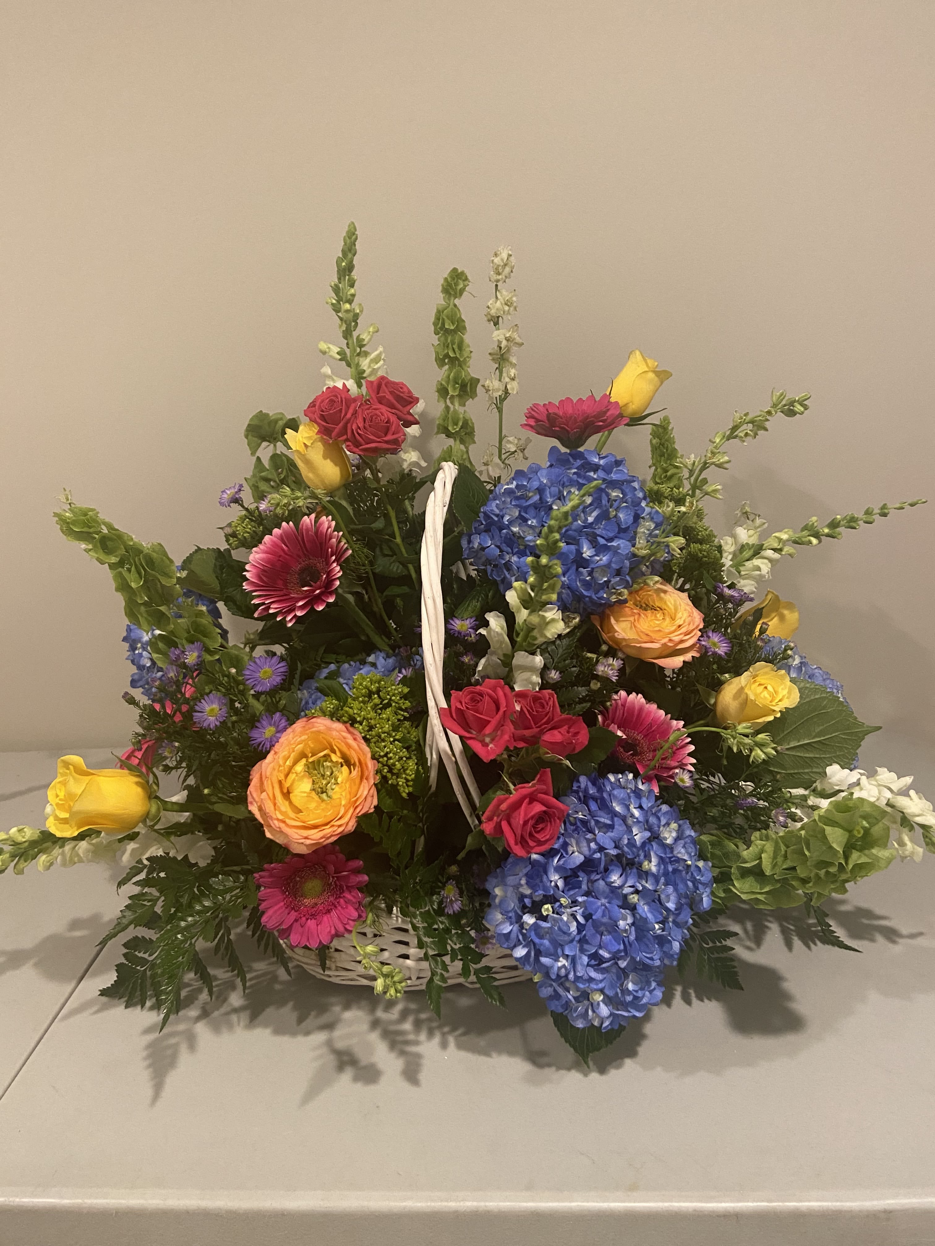 Basket arrangement with blue hydrangeas, roses, gerbera daisies, and yellow tulips