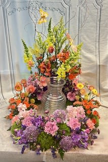 Large colorful floral arrangement around a silver vase