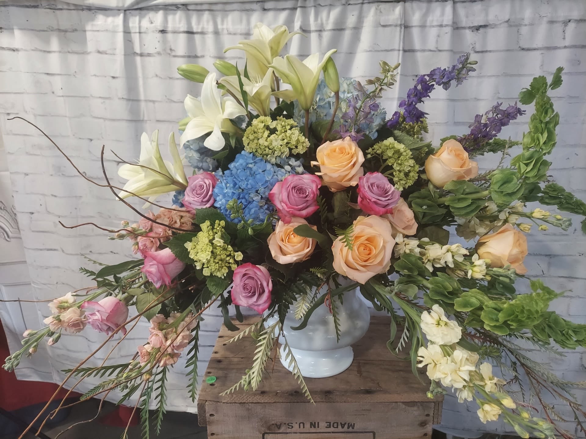 Large mixed bouquet with roses, lilies, hydrangeas, and delphinium in a white vase