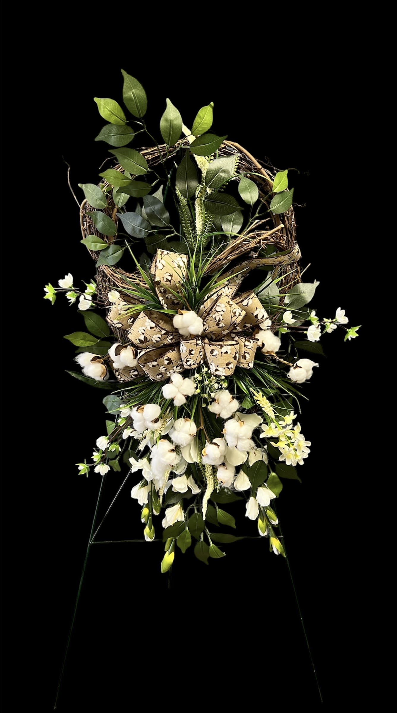 Cotton Grace Silk Standing Spray - Honor a loved one with the timeless elegance of our Cotton Grace Silk Standing Spray. Designed with lifelike silk blooms, delicate cotton accents, and lush greenery, this piece brings a soft and comforting presence to any service. The cascading design is complemented by a premium cotton-themed ribbon, symbolizing purity, warmth, and peace.  This lasting tribute is perfect for families who want a keepsake that will remain beautiful long after the service.