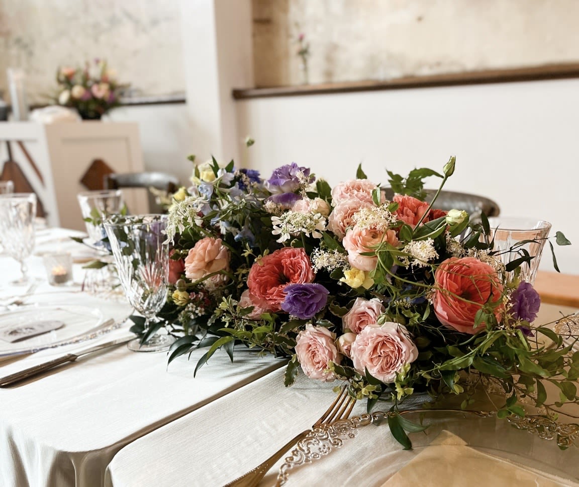 Low floral centerpiece with pink, peach, purple, and white blooms on a table