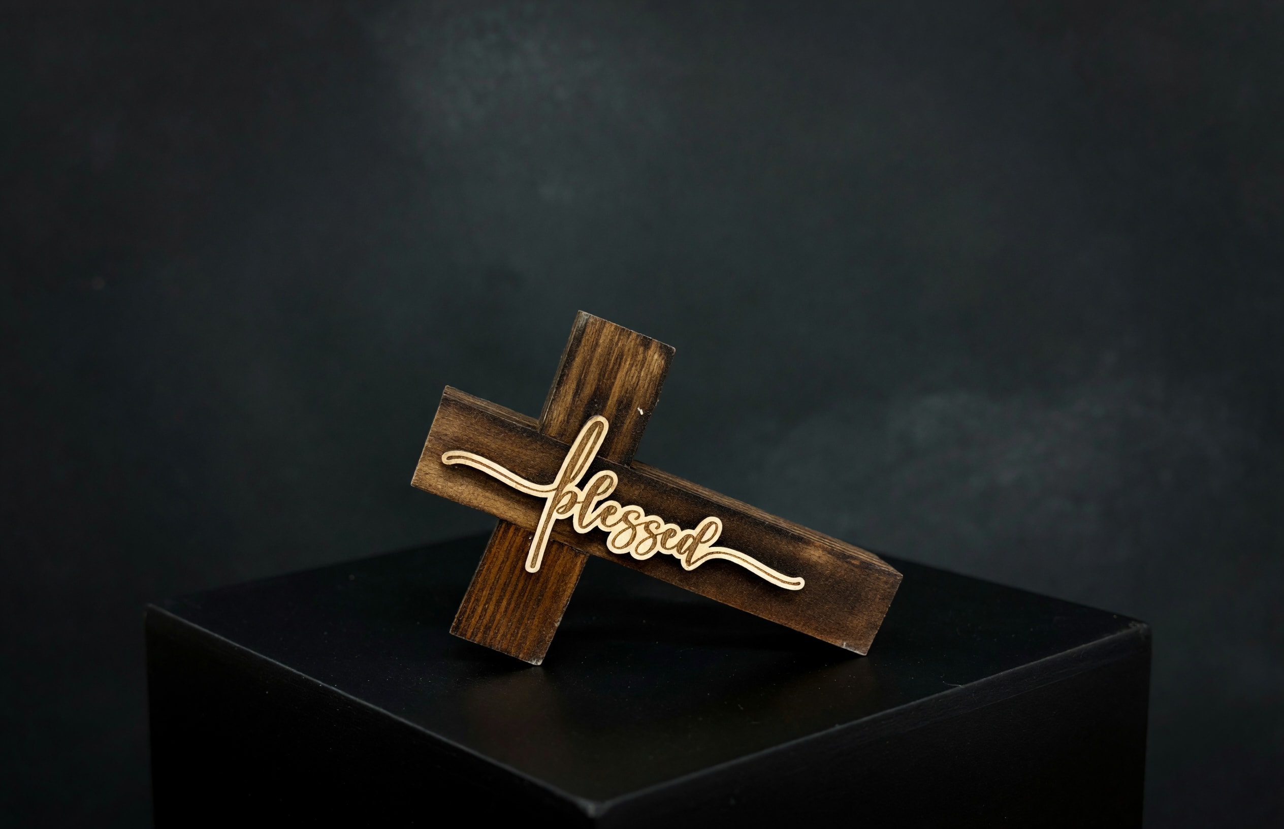 Wooden cross sign with the word blessed on a dark pedestal