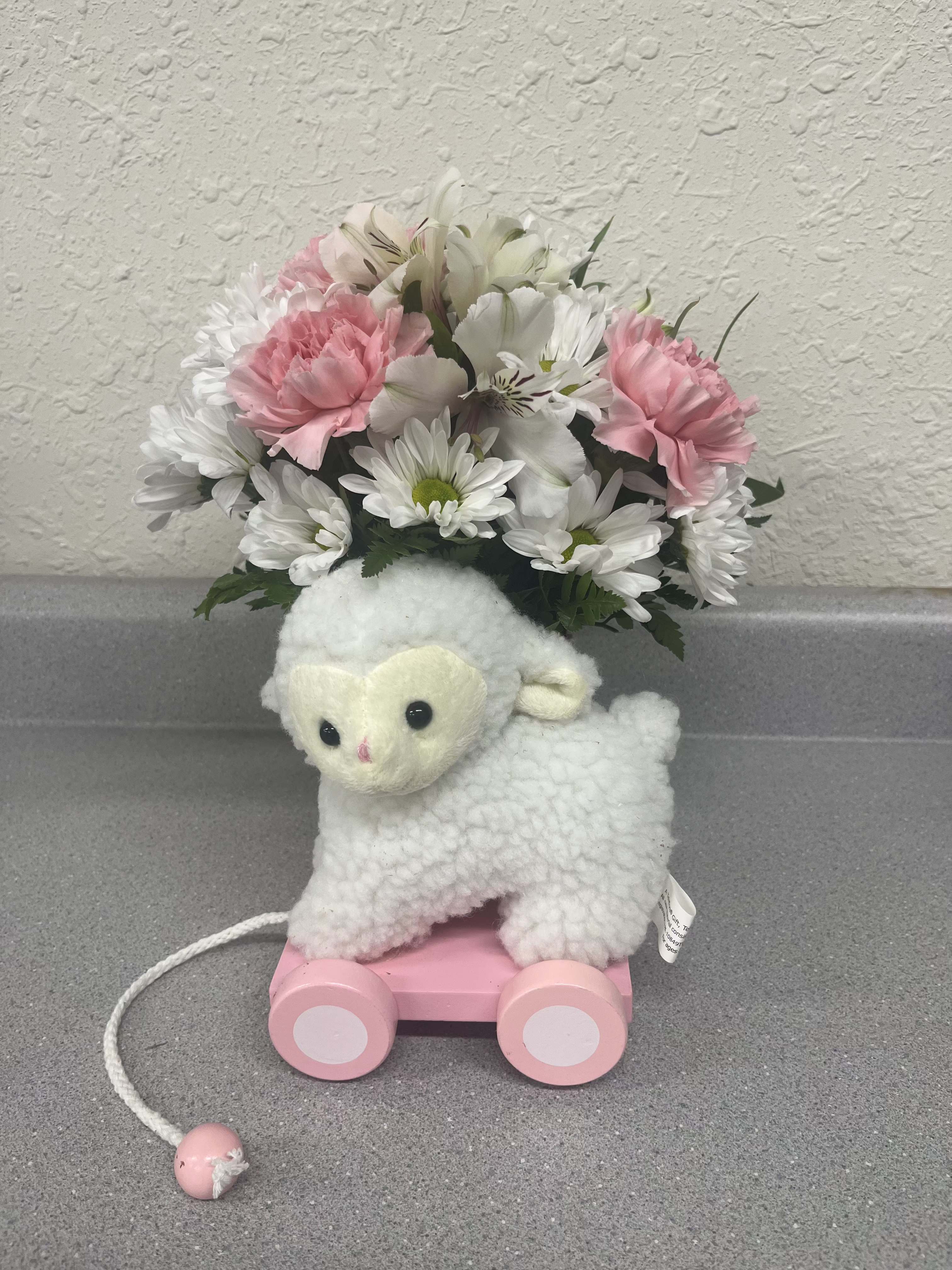 Plush lamb toy with a pink wheeled base and a bouquet of pink and white flowers