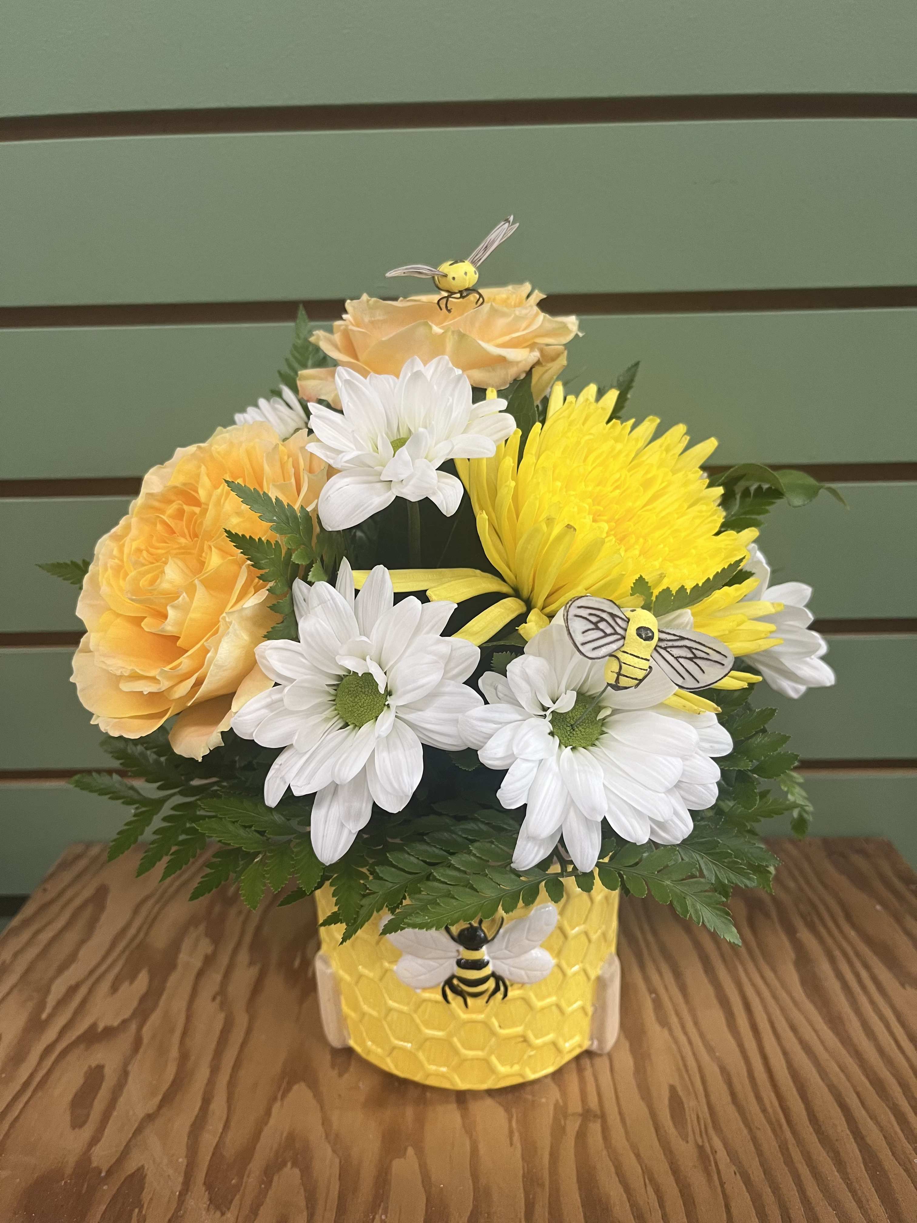 BEEutiful Bouquet - Sunlit yellow roses and bright yellow chrysanthemums mingle with crisp white daisies in a compact, rounded flower arrangement. The playful bee accents and honeycomb-patterned ceramic pot make this floral piece feel whimsical and garden-fresh, so the person you're sending it to will notice the thoughtfulness the moment it arrives.  Ideal for seasonal celebrations, birthdays, thank you's, cheerful get-wells, or simply saying "I'm thinking of you," this arrangement is ready to display on arrival-no fuss required. For best enjoyment, keep in a cool spot away from direct sun and refresh the water as needed to prolong the life of the blooms.