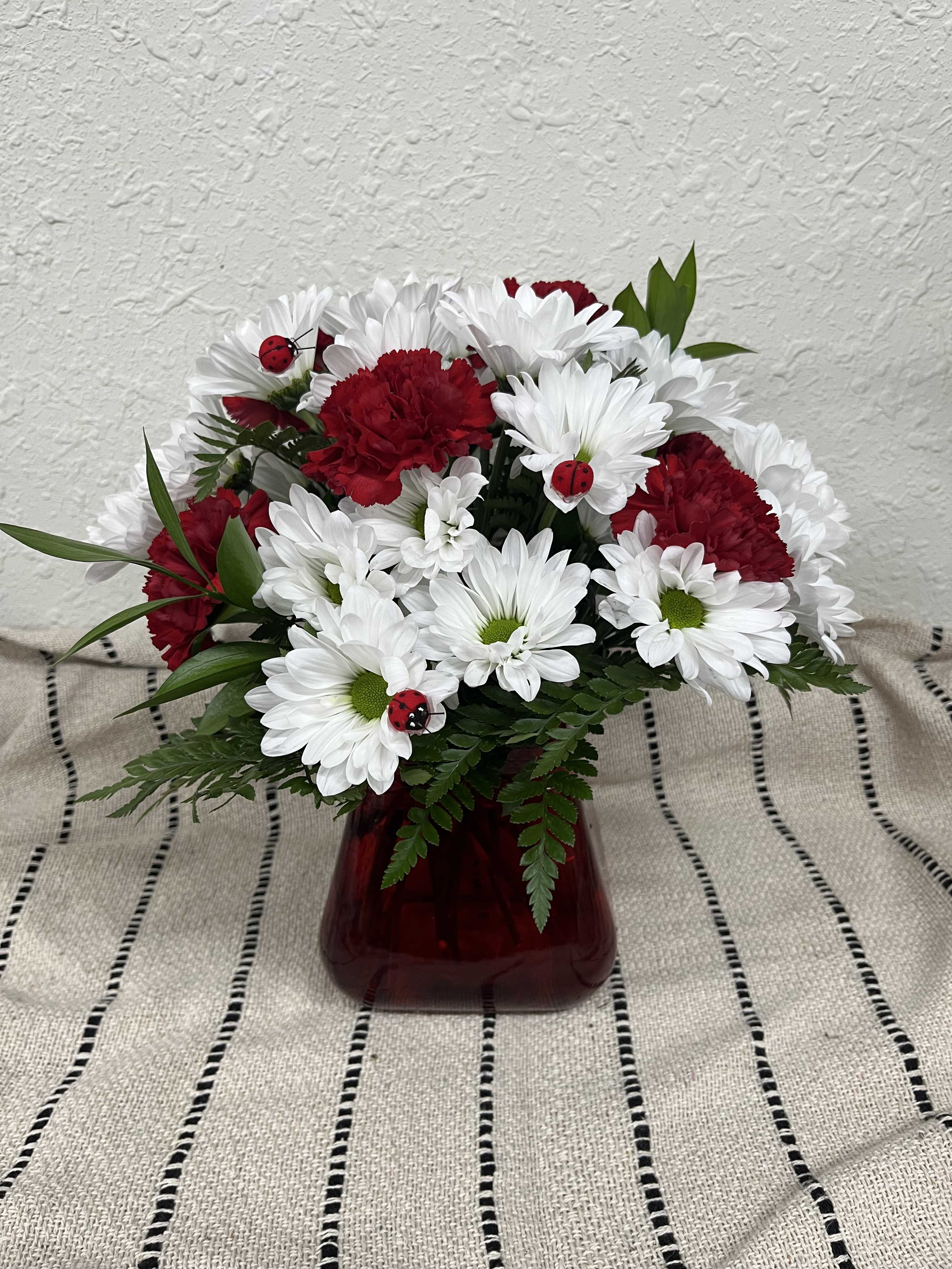 Red carnations and white daisies in a red vase with small ladybug decorations