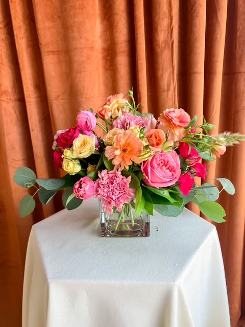 Mixed pink and peach flower arrangement in a square glass vase