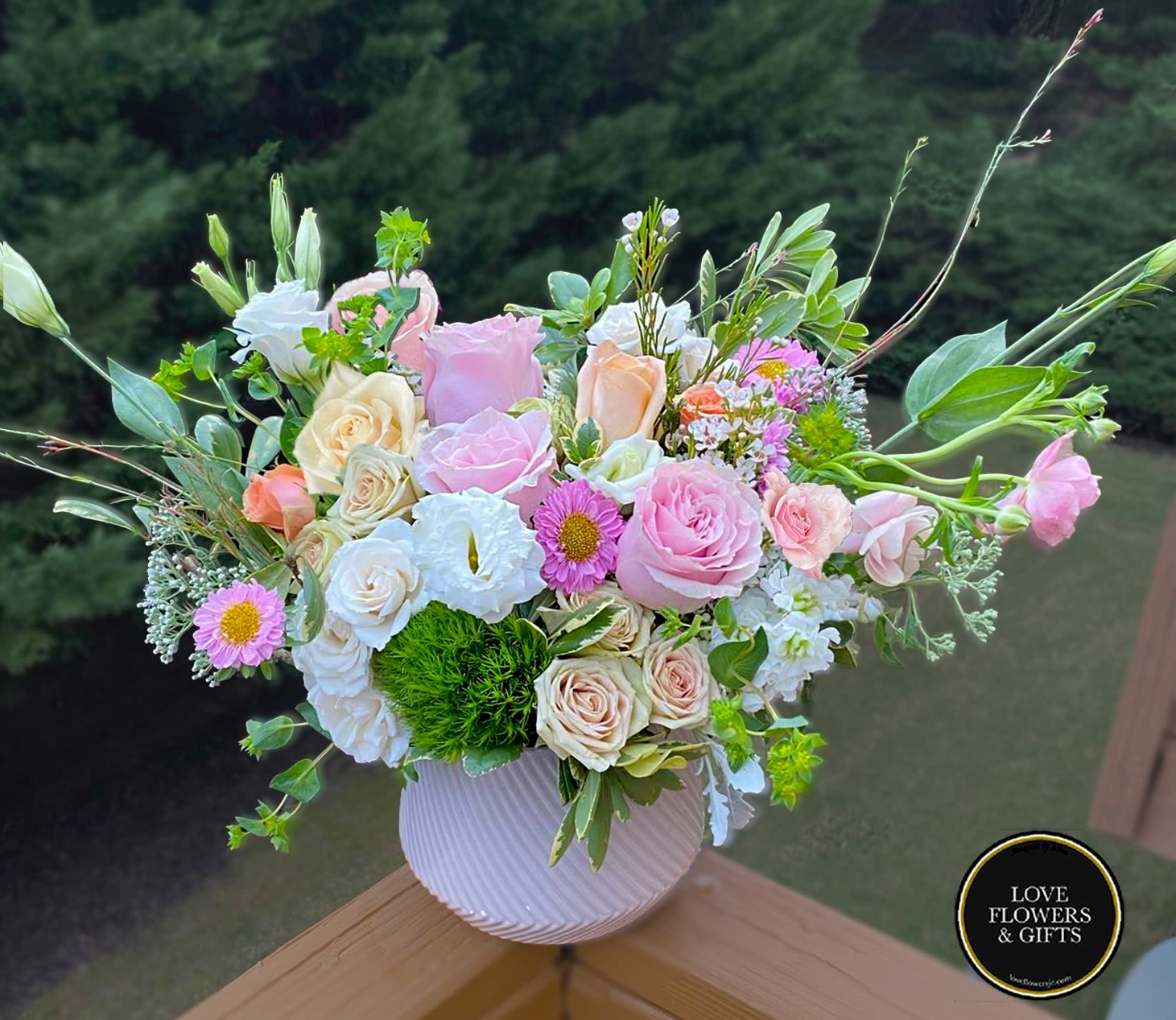 Pastel arrangement of pink roses, cream blooms, and daisies in a white round ceramic vase