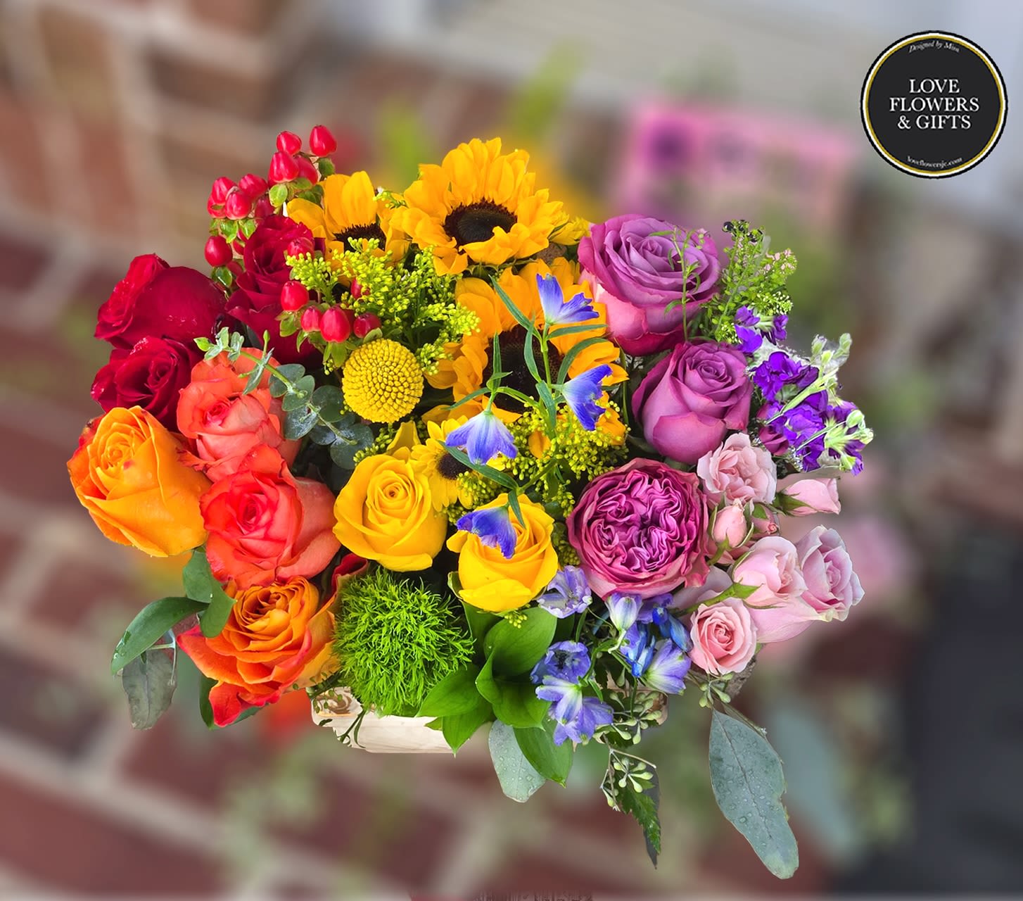 Bright mixed bouquet with yellow sunflowers, multicolor roses, and purple and blue accent flowers