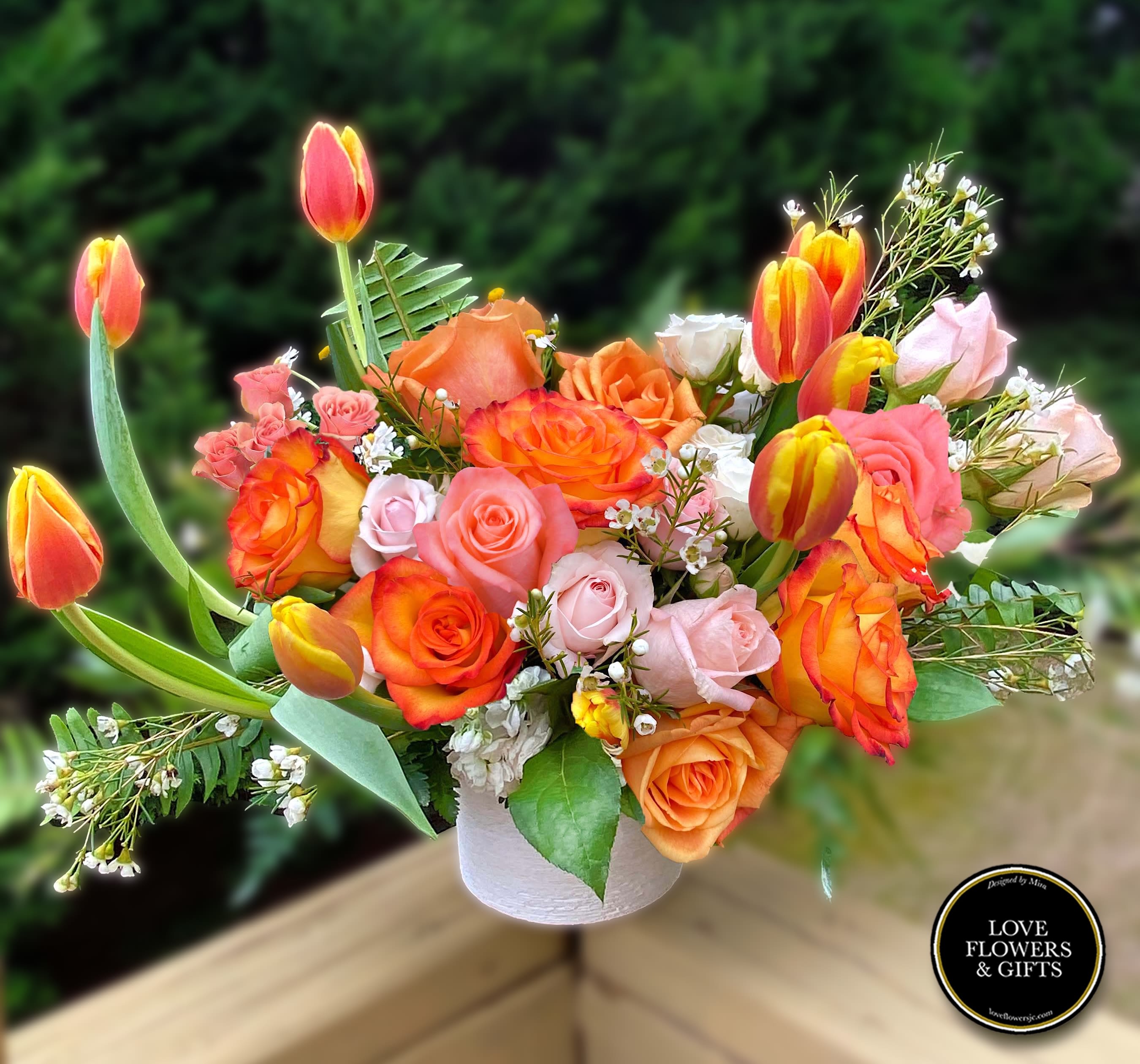 Arrangement of orange and pink roses with yellow-orange tulips in a white vase