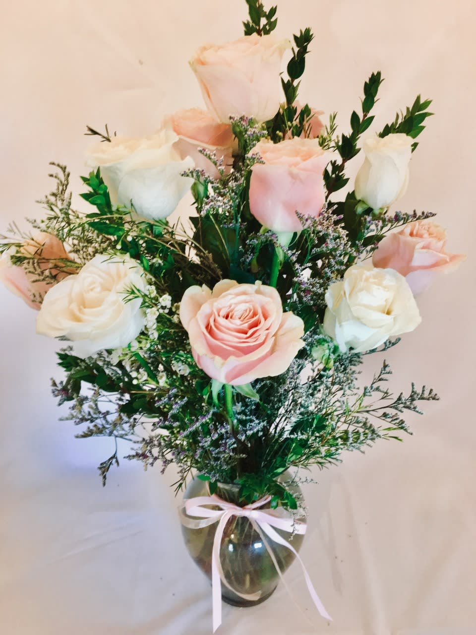Arrangement of pink and white roses with filler flowers in a clear glass vase tied with a ribbon