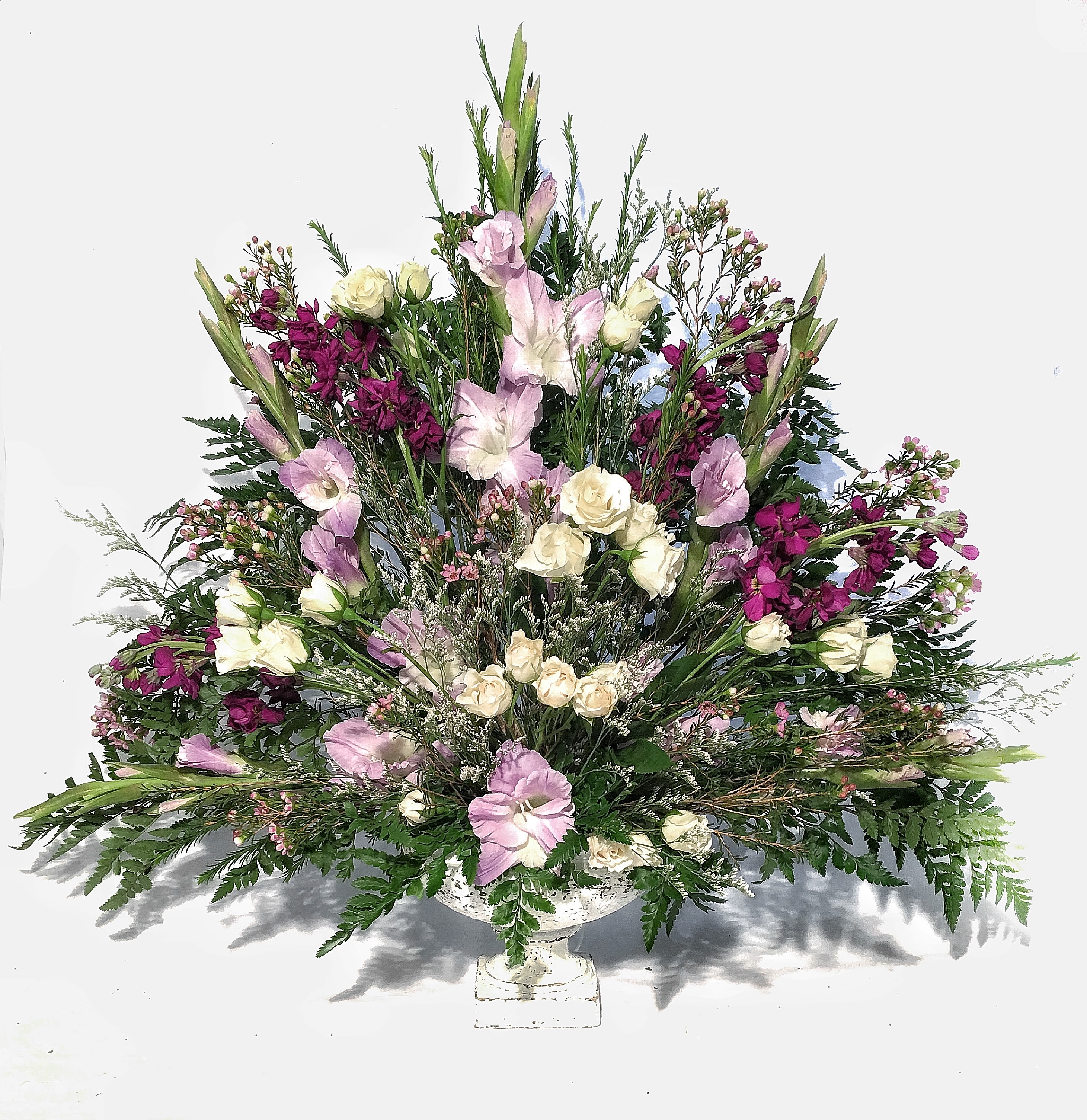 Fan-shaped arrangement of white spray roses and lavender flowers in a white pedestal bowl